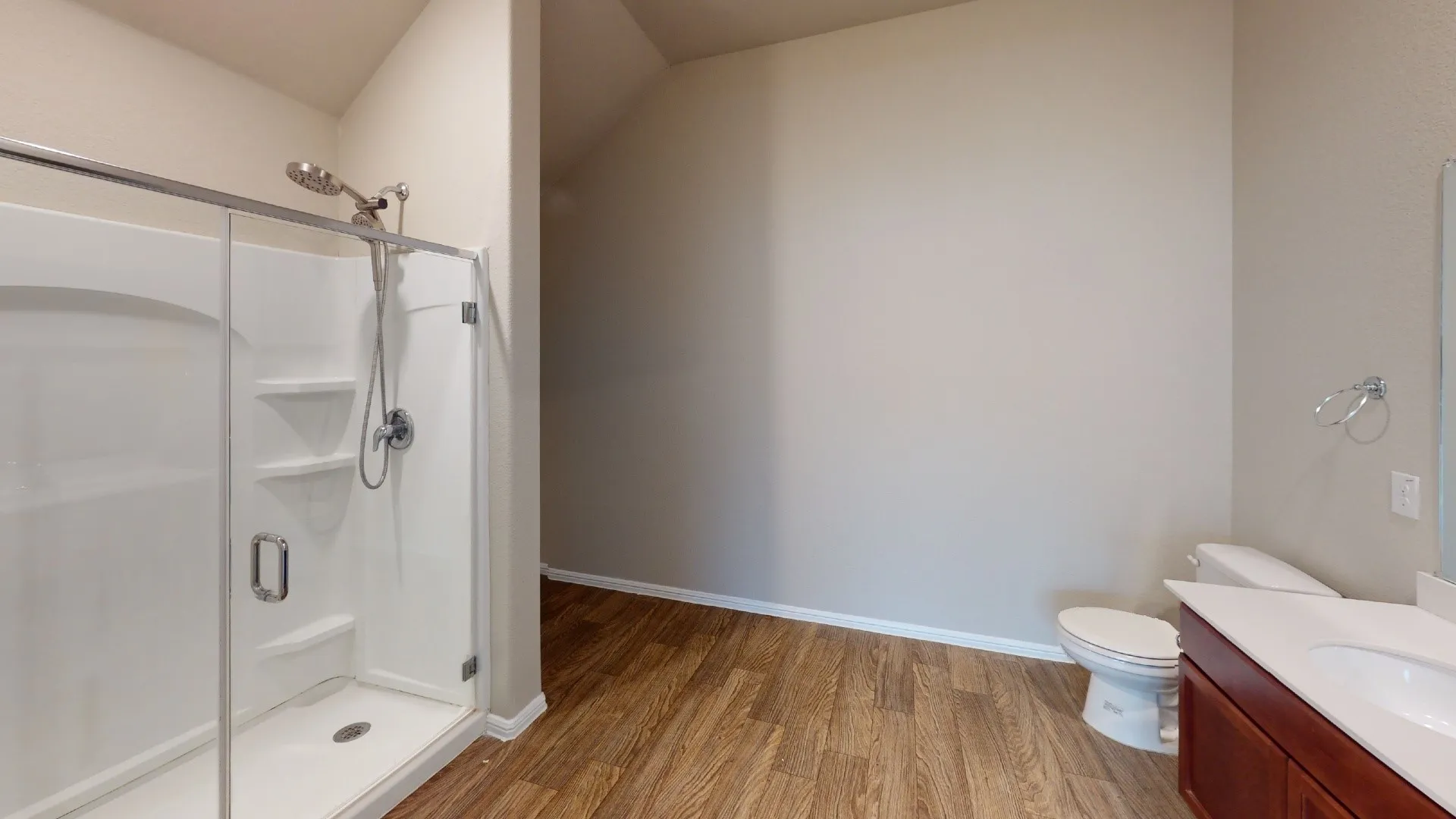 Glass-enclosed shower with built-in shelving, wood-finish flooring, and a single vanity with a white countertop