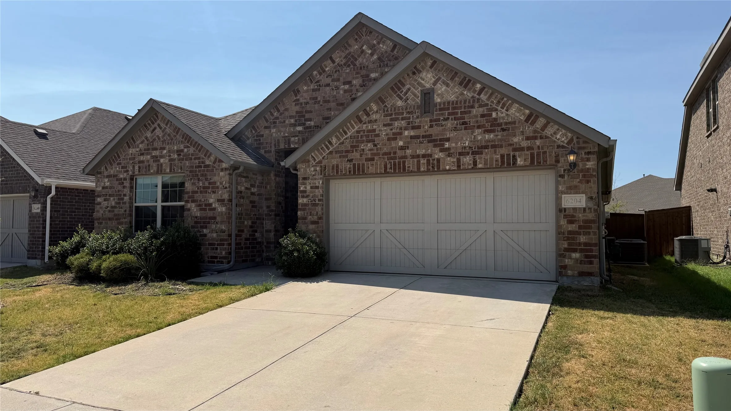 Brick exterior with a gabled roofline, concrete driveway, and attached two-car garage with decorative paneling