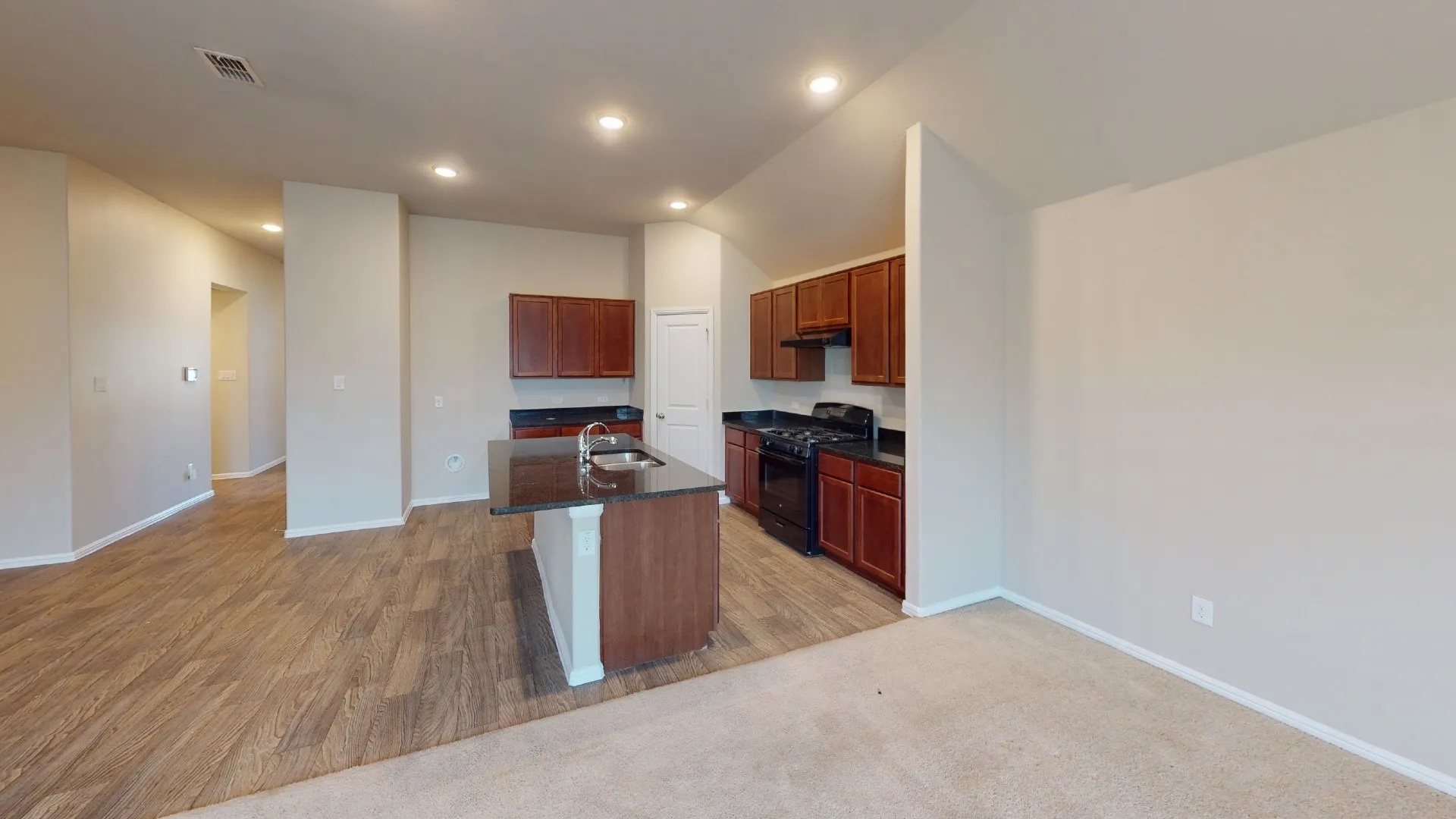Wood-finish flooring, recessed lighting, kitchen island with sink and dark countertop, dark wood-finish cabinetry, and black appliances