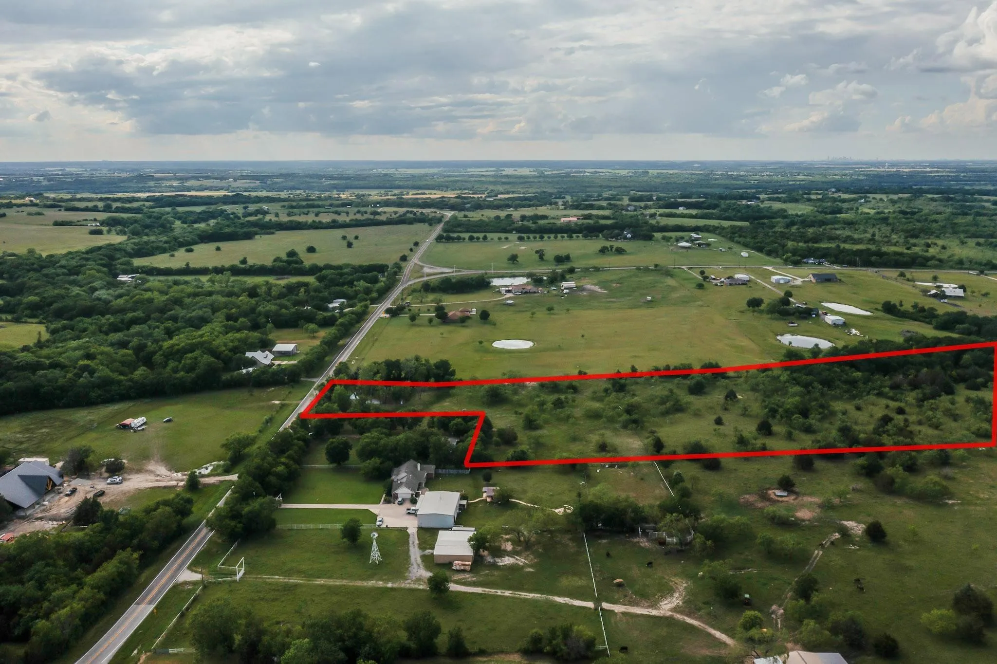 Expansive rural acreage with scattered trees, bordered by a paved road