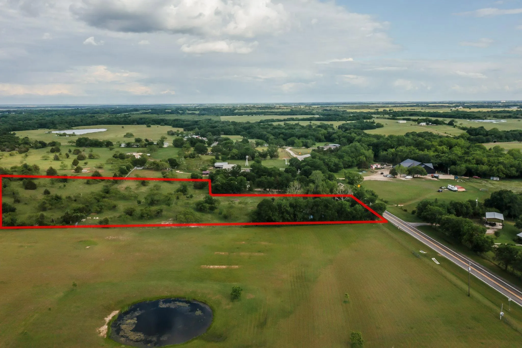 Expansive land parcel featuring open fields, scattered mature trees, and direct road frontage