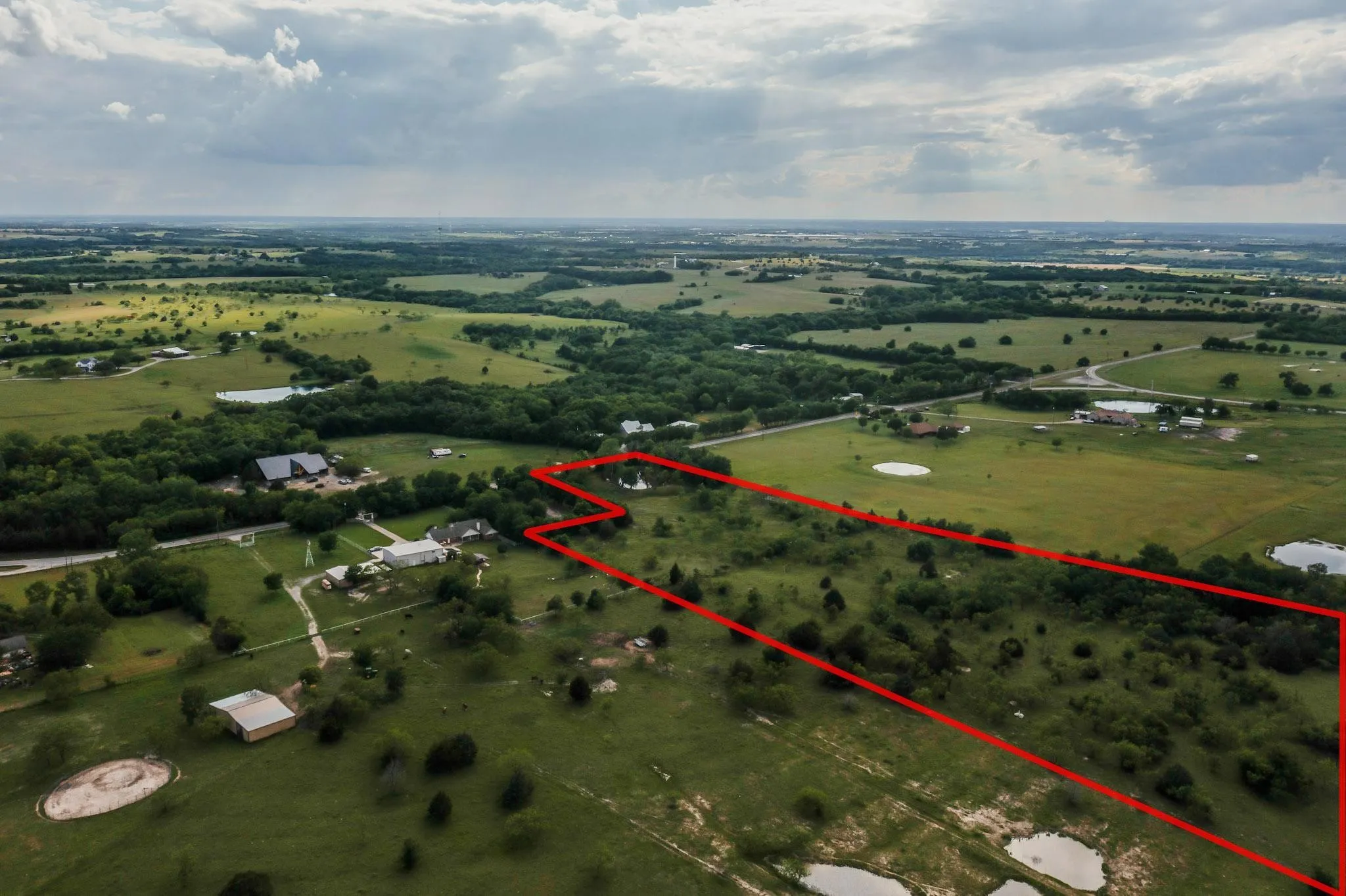 Expansive acreage featuring a perimeter marked by a red boundary, varied tree coverage, and distant rural landscape