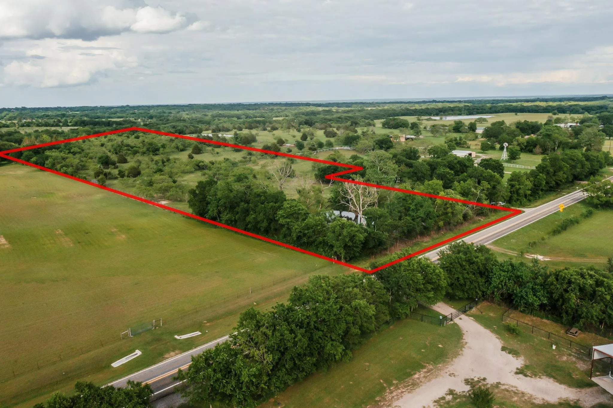 Expansive rural acreage featuring green pastures, mature trees, and direct road frontage