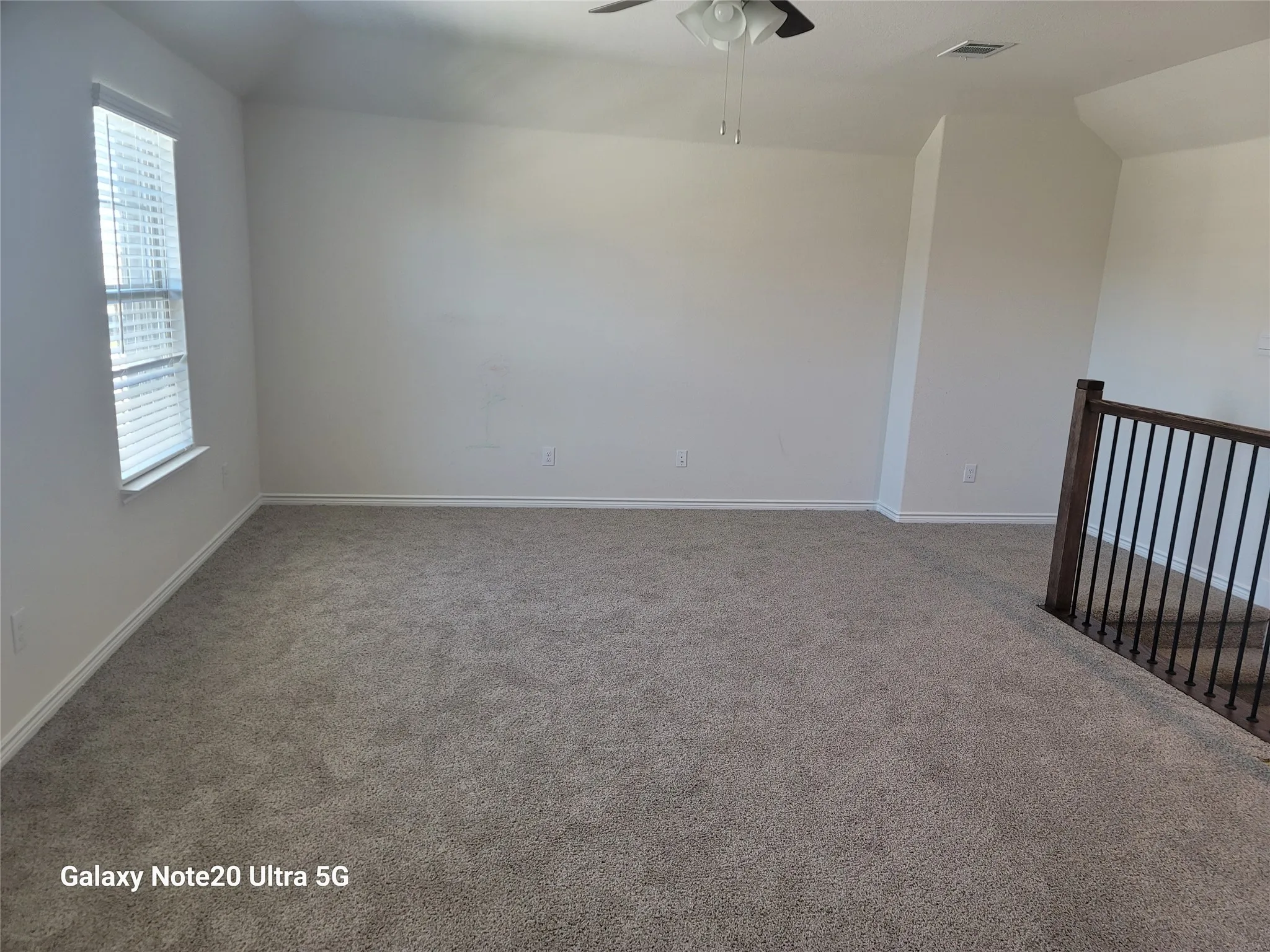 Carpeted room with a ceiling fan, a window with blinds, and a wood and iron railing