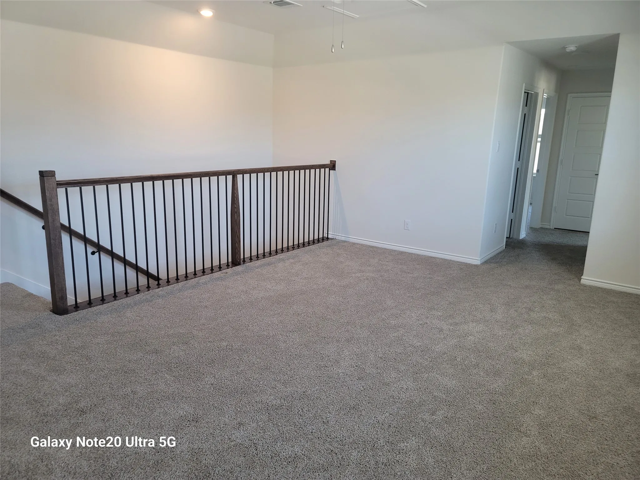 Carpeted landing featuring dark wood-finish railing with black balusters, recessed lighting, and ceiling fan