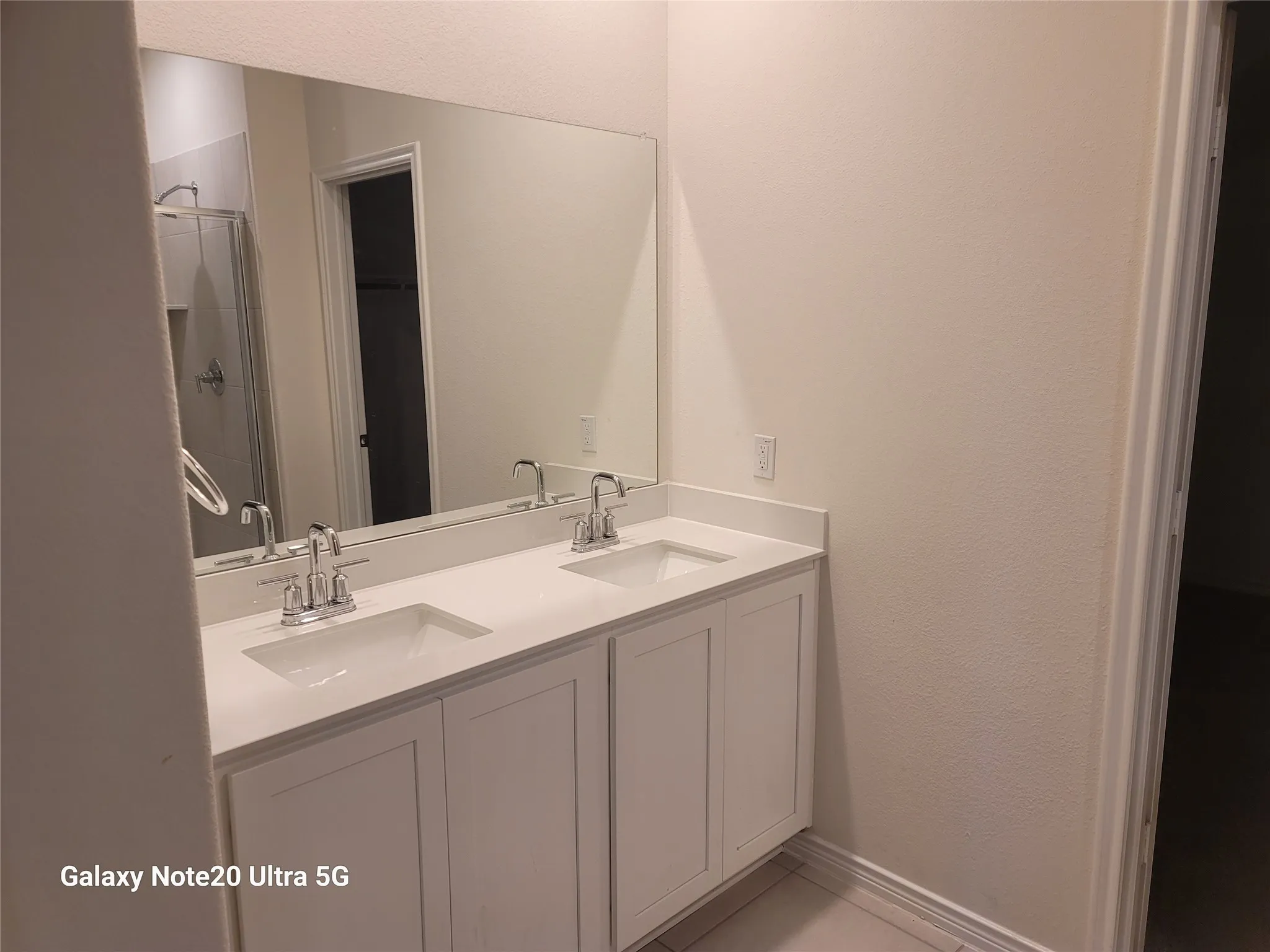 Dual vanity with integrated sinks, chrome fixtures, white cabinetry, and a large wall-mounted mirror