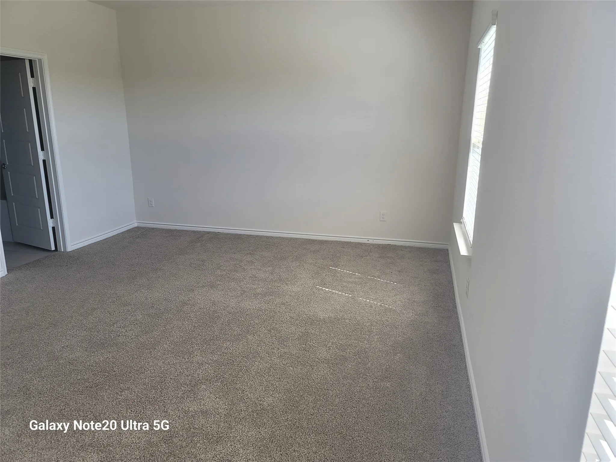 Neutral tone wall paint, light gray carpeting, white trim, and a window with horizontal blinds
