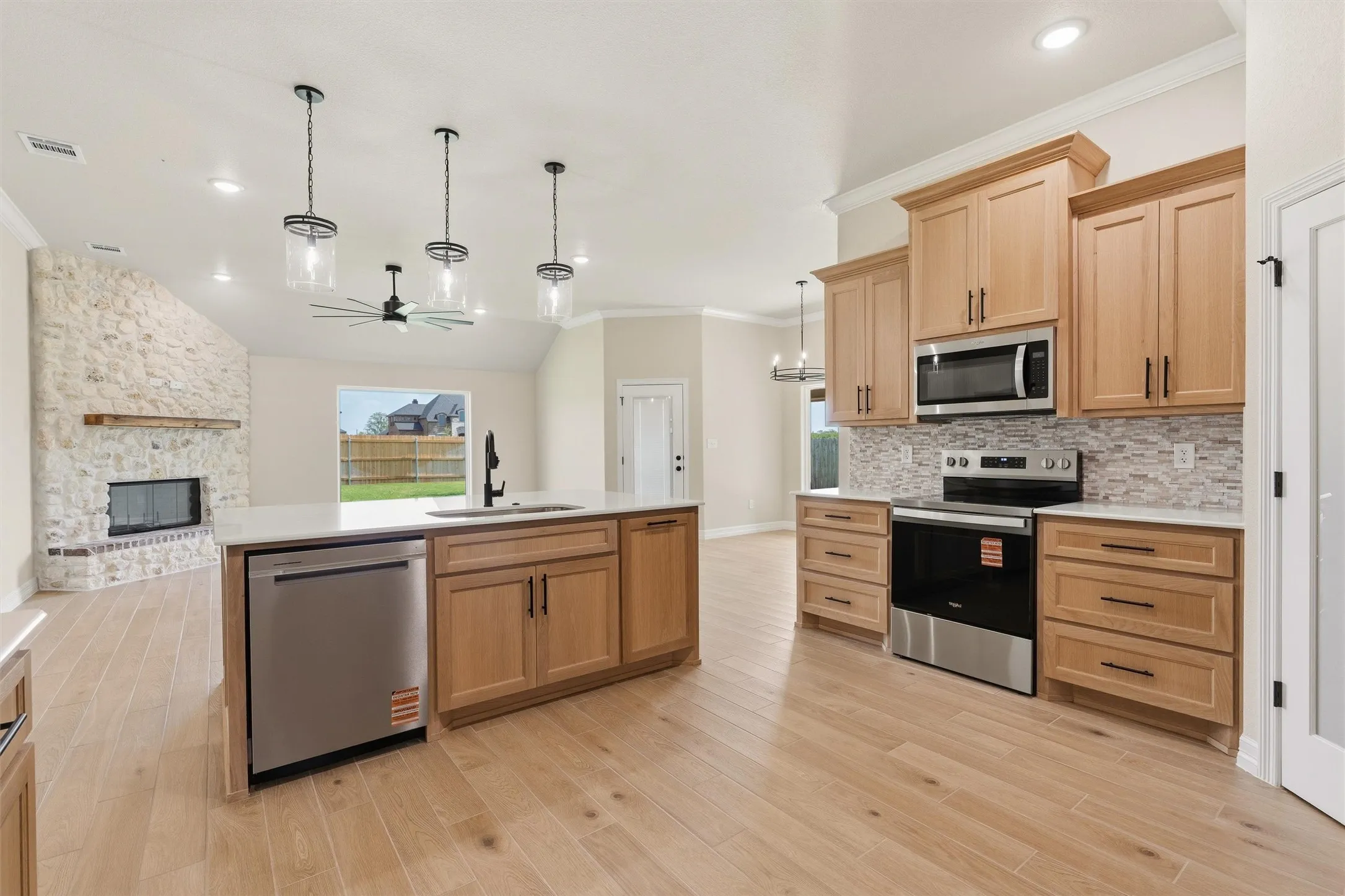 Expansive kitchen featuring light wood-finish cabinetry, stainless steel appliances, a center island with sink, and wood-finish flooring