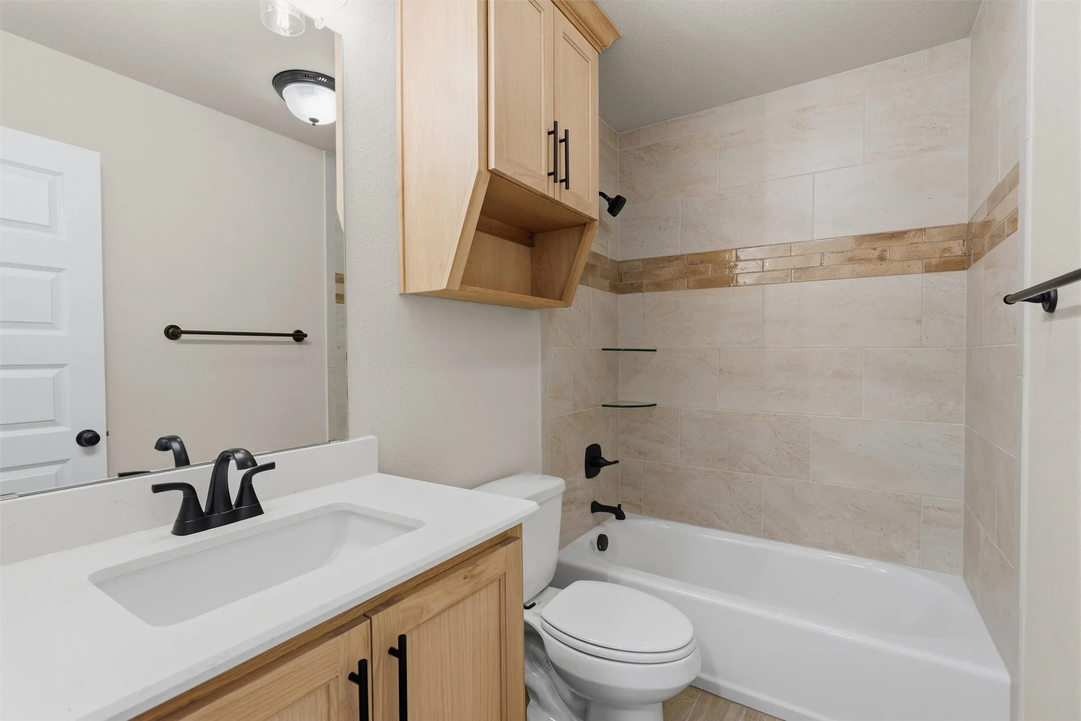 Bathroom featuring a vanity with a white countertop and undermount sink, matte black faucet, light wood-finish cabinetry, and a full bathtub with tiled surround