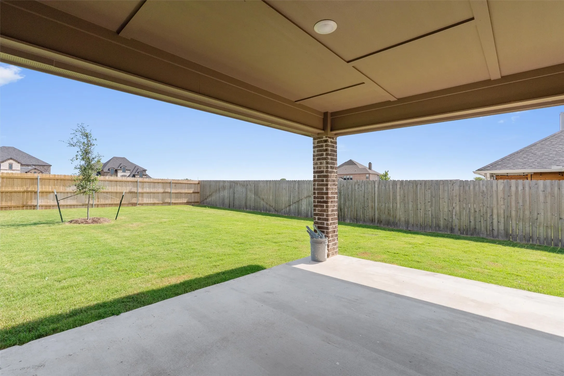 Expansive backyard with a covered concrete patio, brick column, and wood privacy fencing