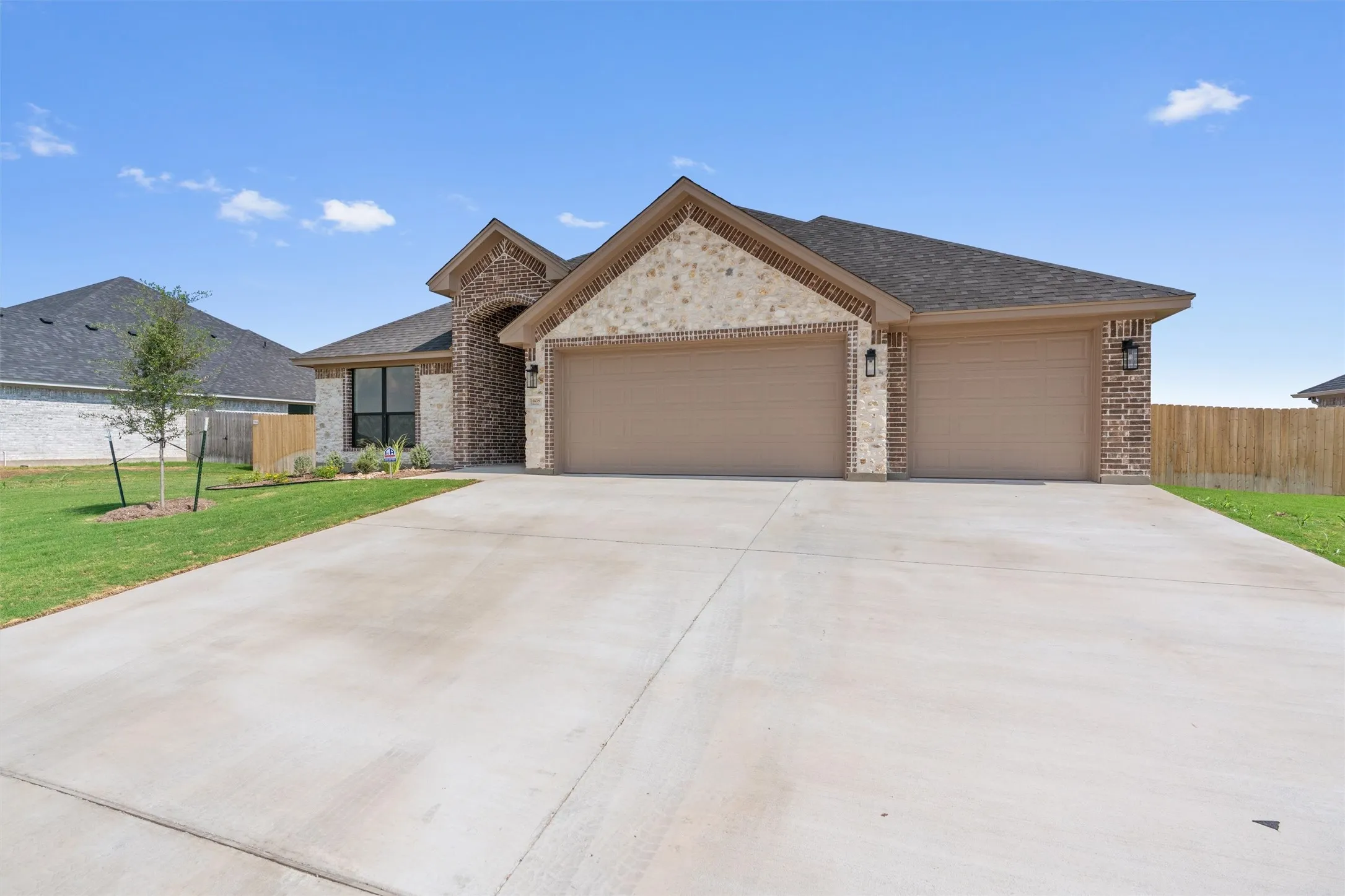 Brick and stone facade, arched entryway, attached two-car garage, concrete driveway, and a manicured lawn