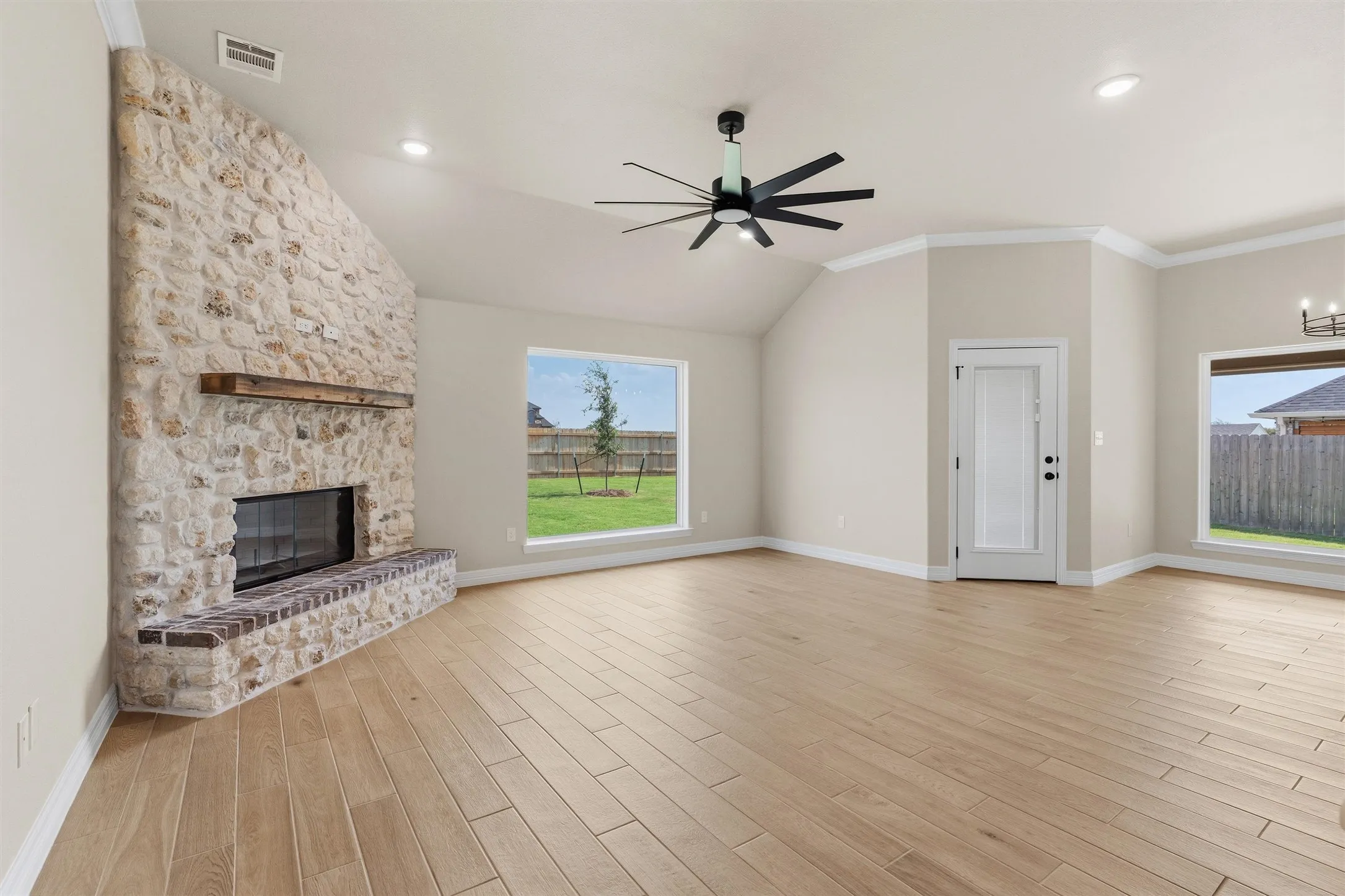 Spacious room featuring a stone-clad fireplace with a wood mantel, light wood-finish flooring, and vaulted ceiling