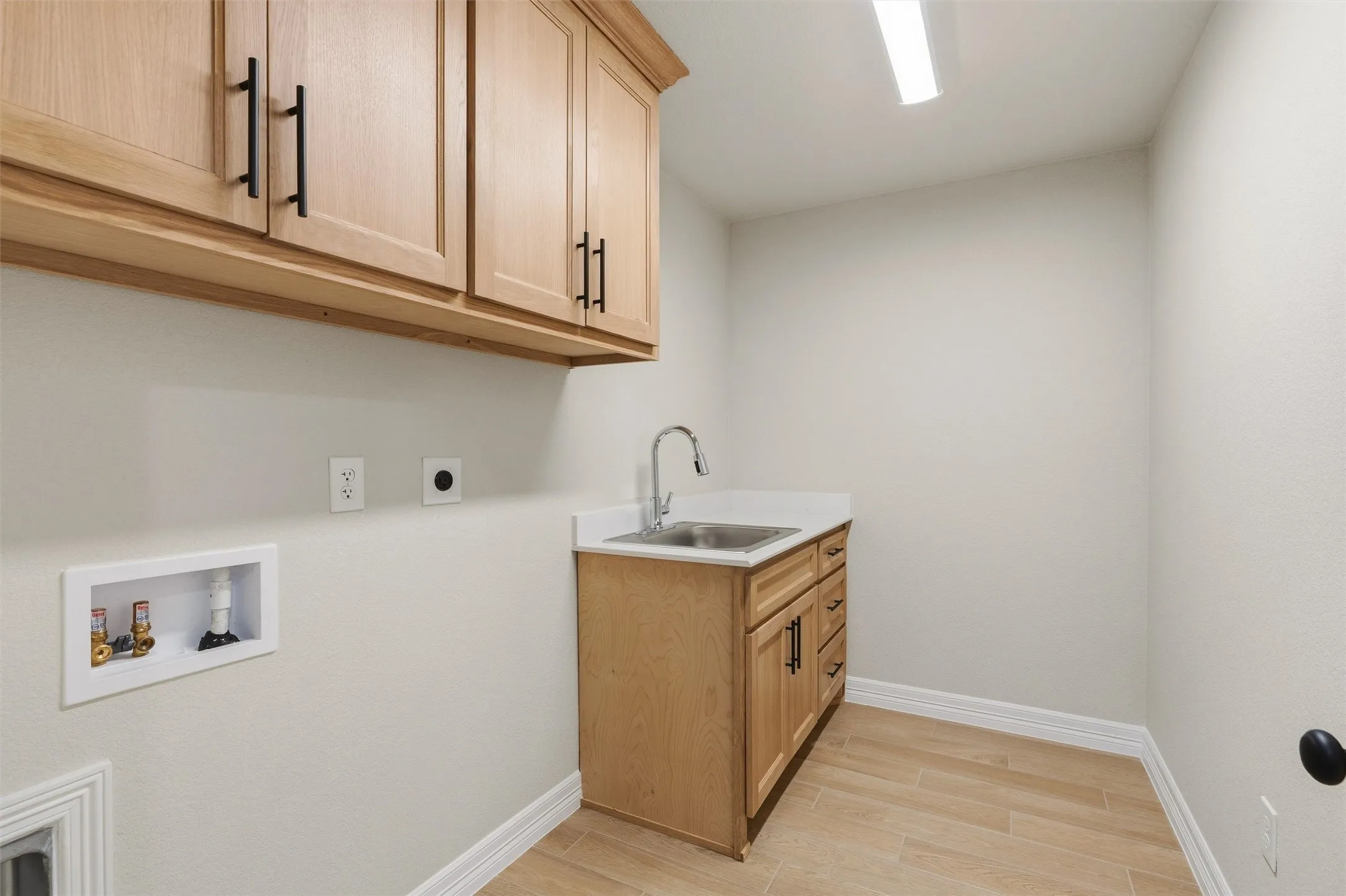 Light wood-finish cabinetry with black hardware, white countertop with an undermount sink, gooseneck faucet, and wood-look tile flooring