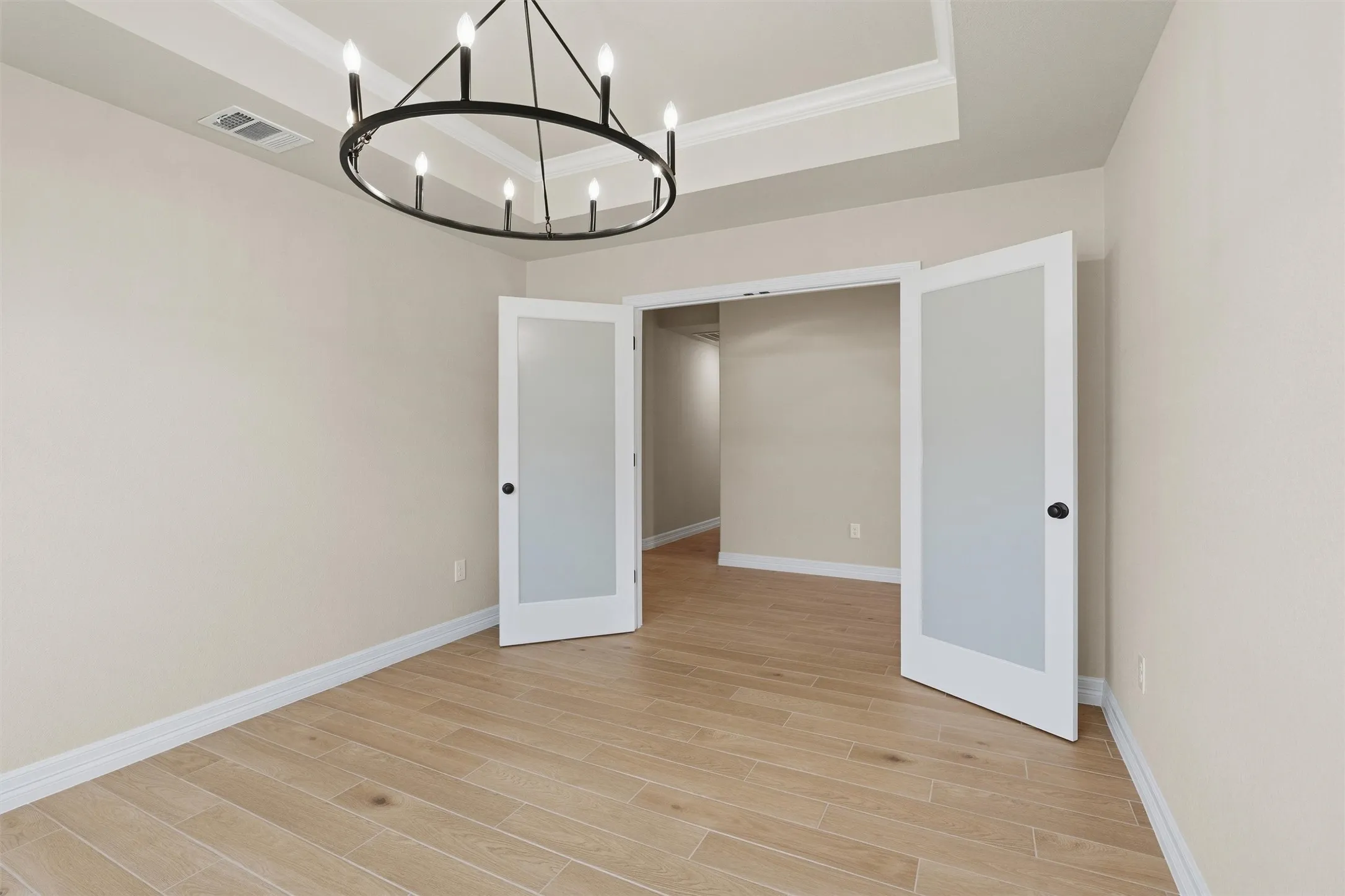Tray ceiling with crown molding, contemporary chandelier, wood-finish flooring, and double French doors with frosted glass panels