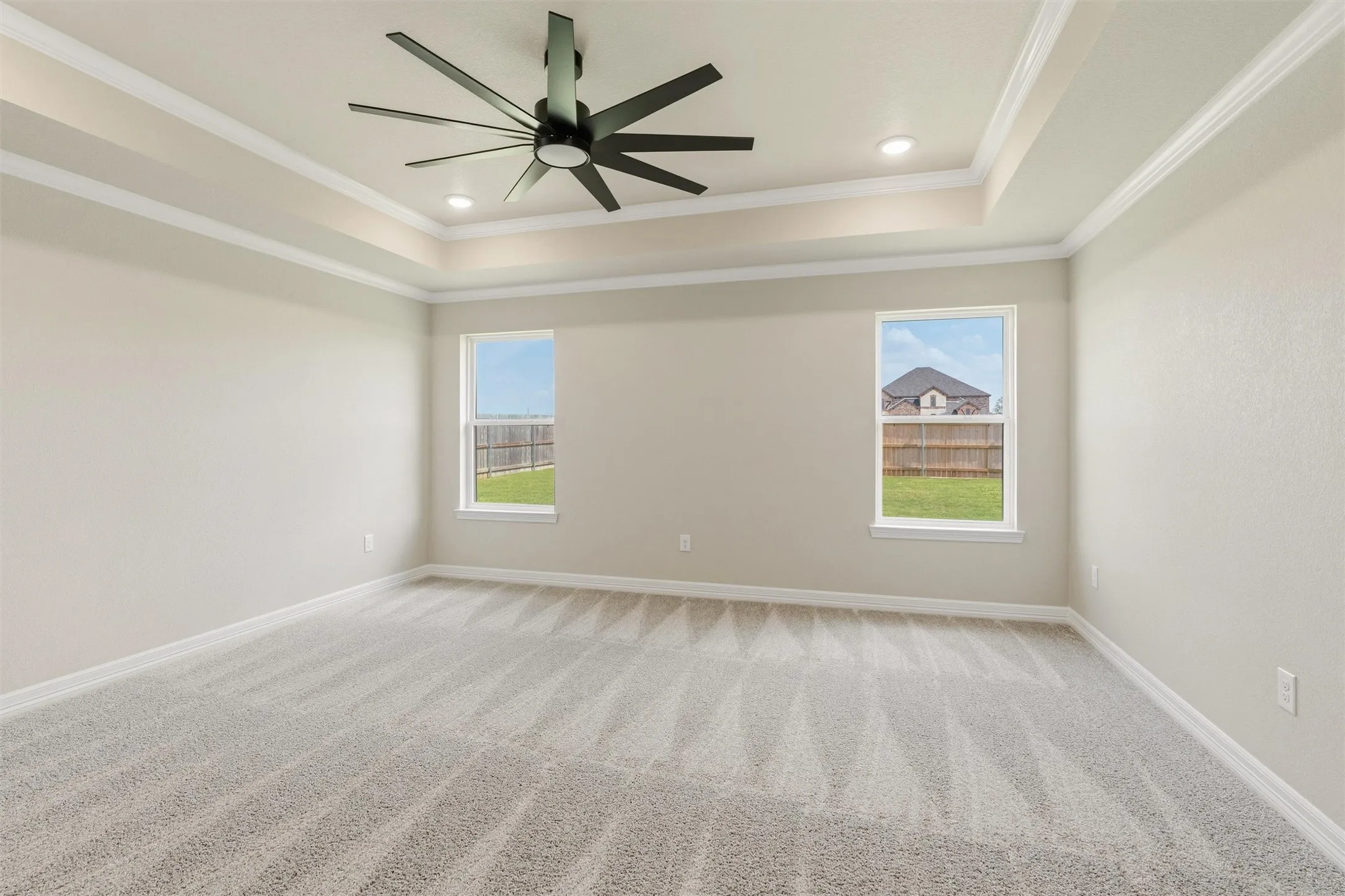 Tray ceiling with recessed lighting, modern ceiling fan, two windows, and light gray wall-to-wall carpeting