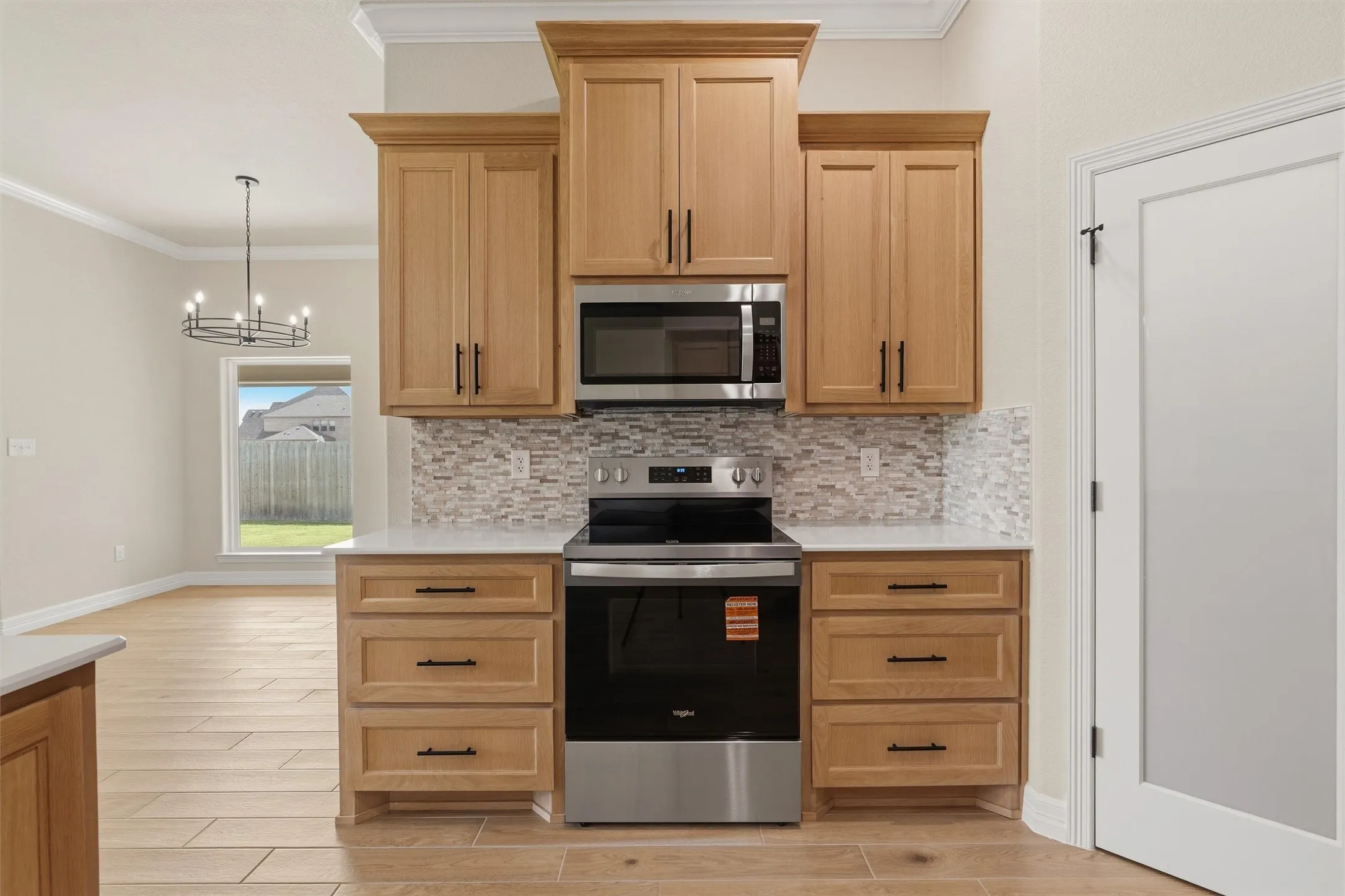 Kitchen featuring light wood cabinetry, stainless steel appliances, white countertops, and a mosaic tile backsplash