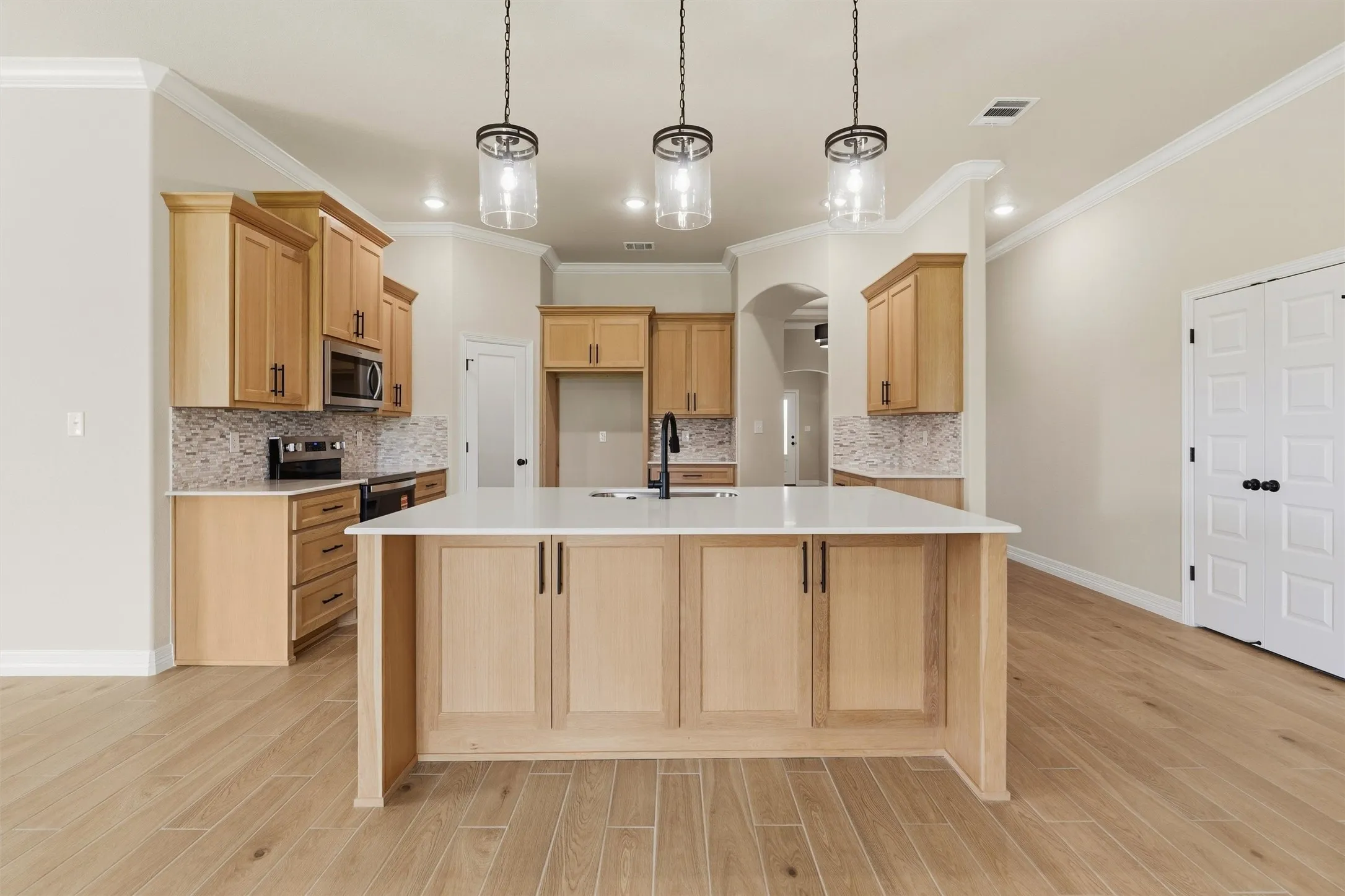 Spacious kitchen featuring an island with white countertop, wood-finish flooring, light wood cabinetry, a tile backsplash, and recessed lighting