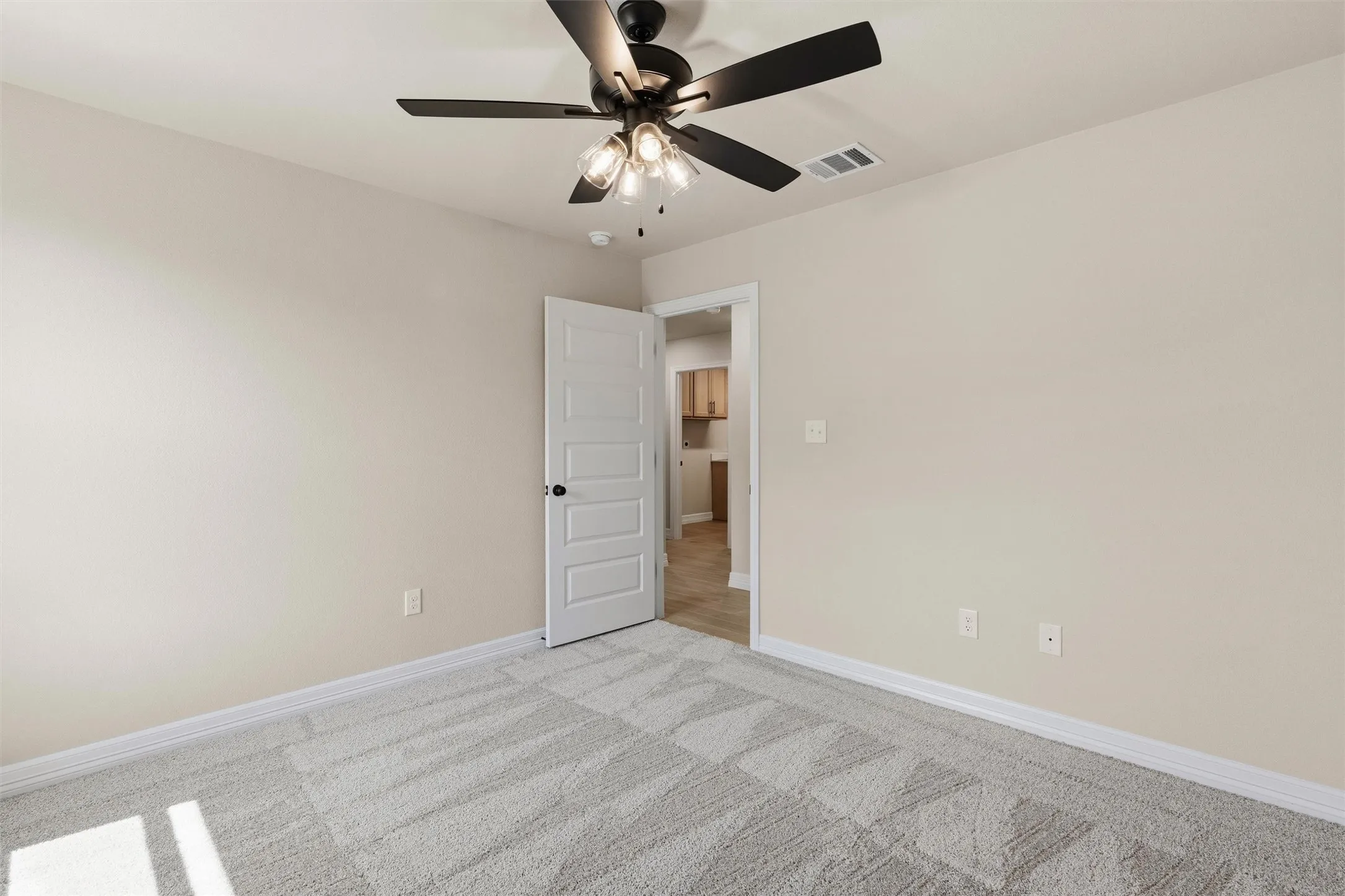 Textured carpet flooring, neutral paint palette, white trim, five-panel interior door, and a ceiling fan with integrated lighting