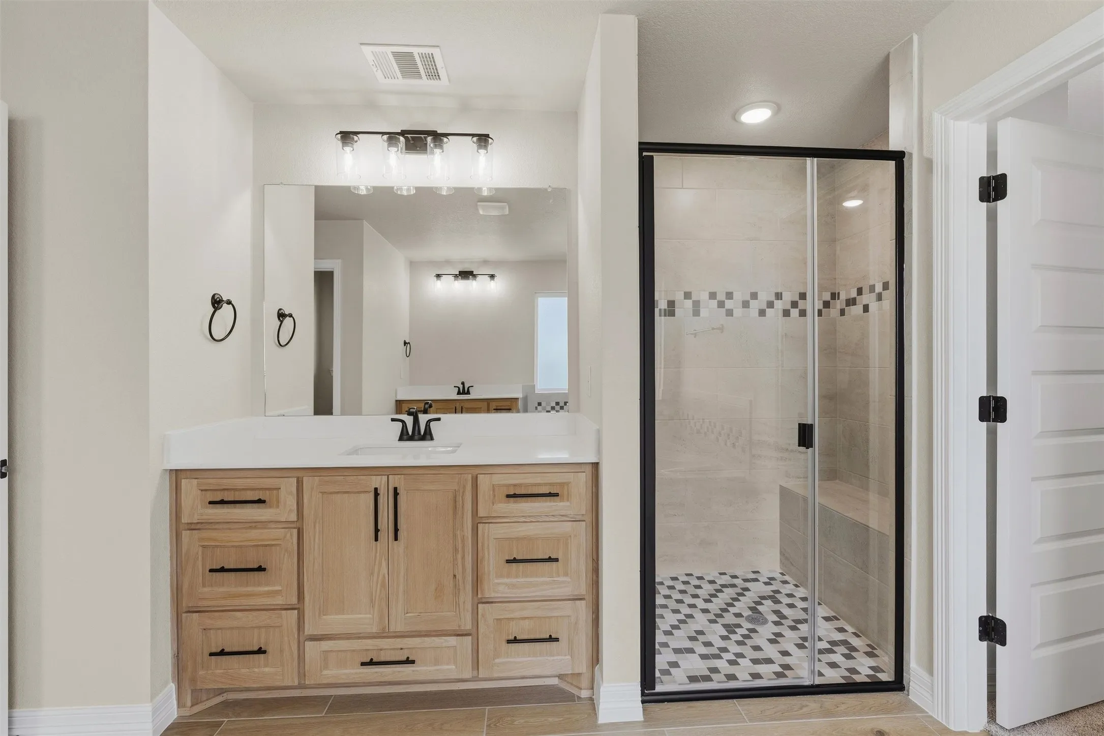 Wood-finish vanity with white countertop, black fixtures, and framed mirror