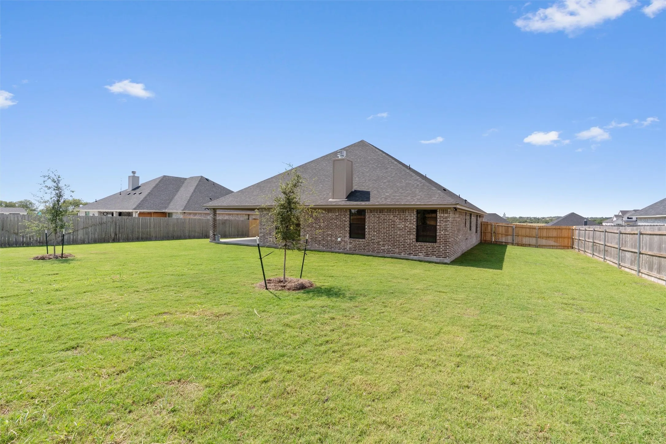Expansive backyard with a manicured lawn, full privacy fencing, and a covered concrete patio