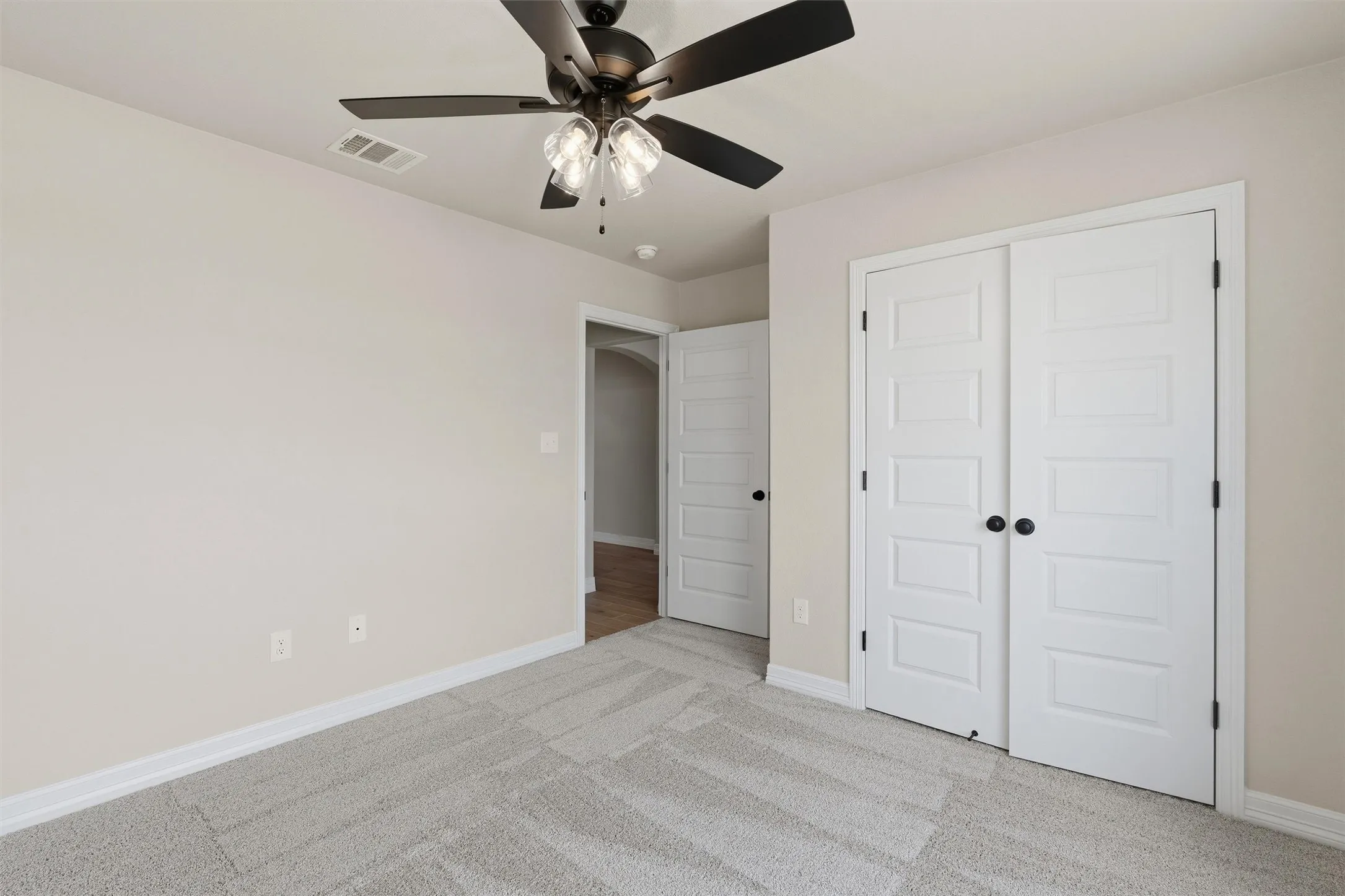 Neutral wall tones, gray carpeting, and a ceiling fan with integrated lighting