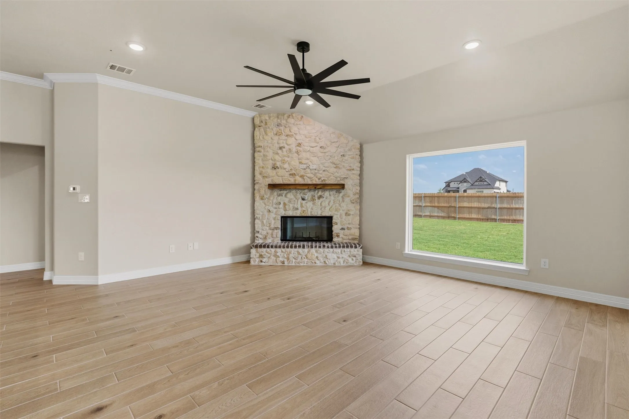 Vaulted ceilings, a stone fireplace with a wood-finish mantel, wood-look flooring, recessed lighting, and a modern ceiling fan with a matte black finish
