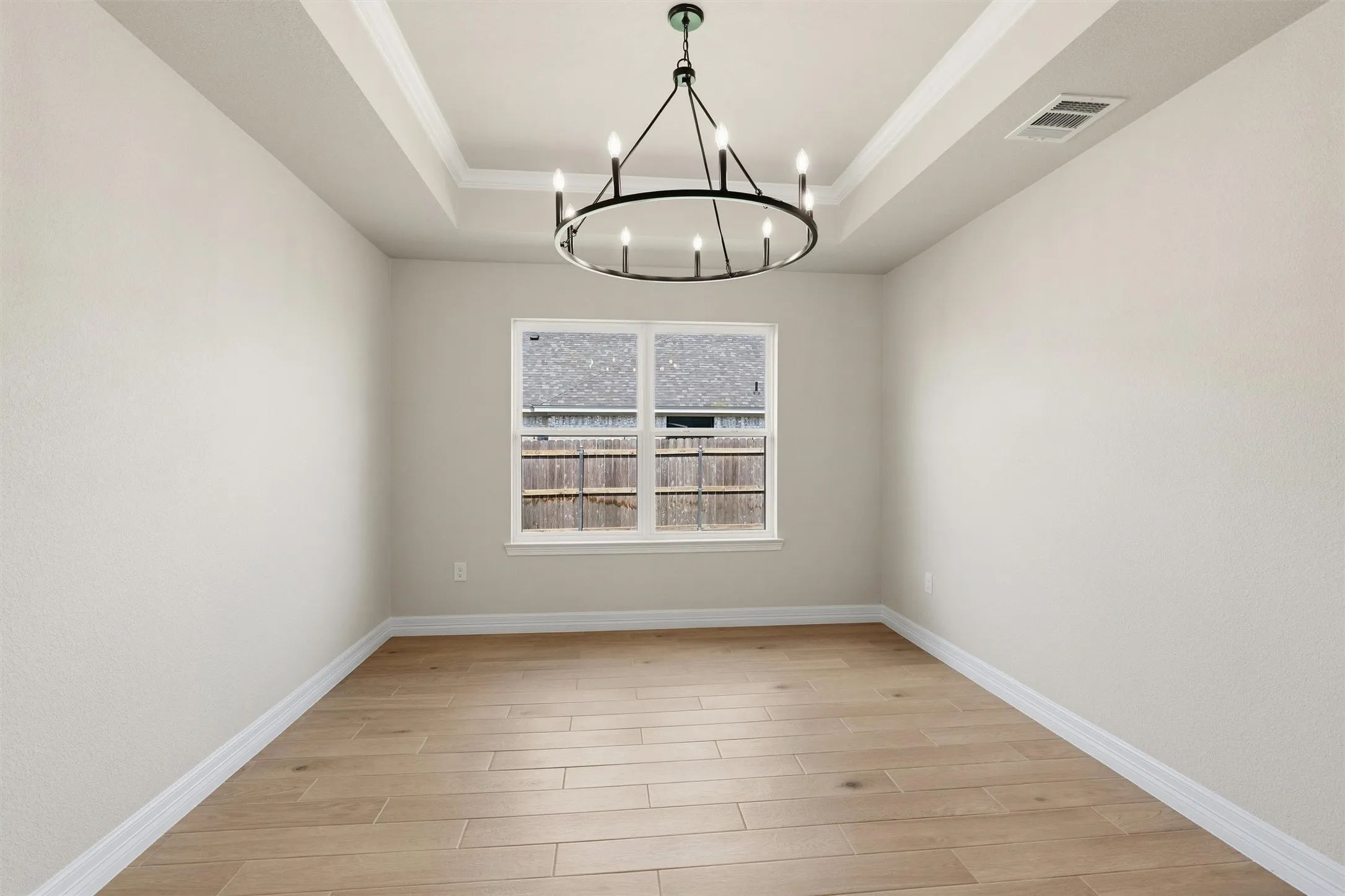 Recessed tray ceiling with crown molding, contemporary chandelier, wood-finish flooring, and a window with white trim