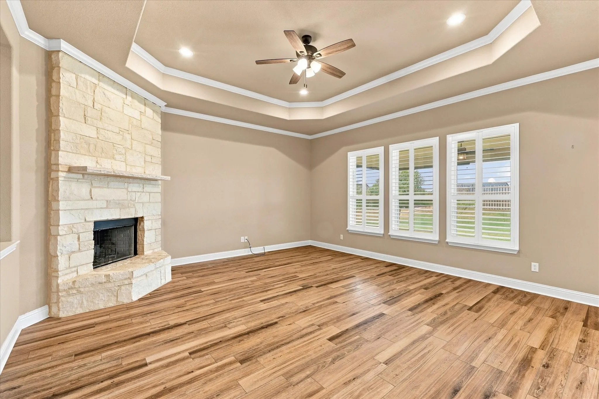 Grand living room with recessed lighting, ceiling fan, wood-look tile, and plantation shutters on windows overlooking back yard.
