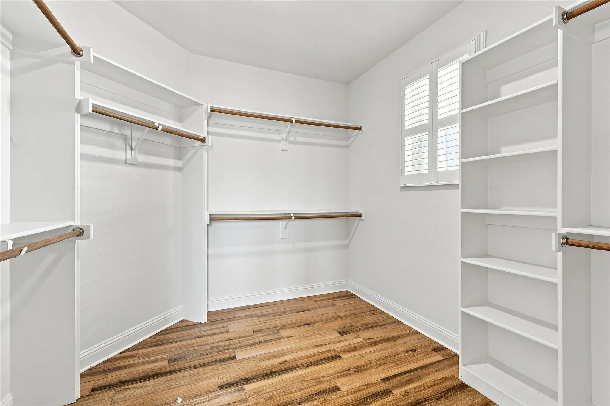Amazing primary closet in back of primary bathroom with built in shelves and a lovely window to brighten choosing the day's outfit.