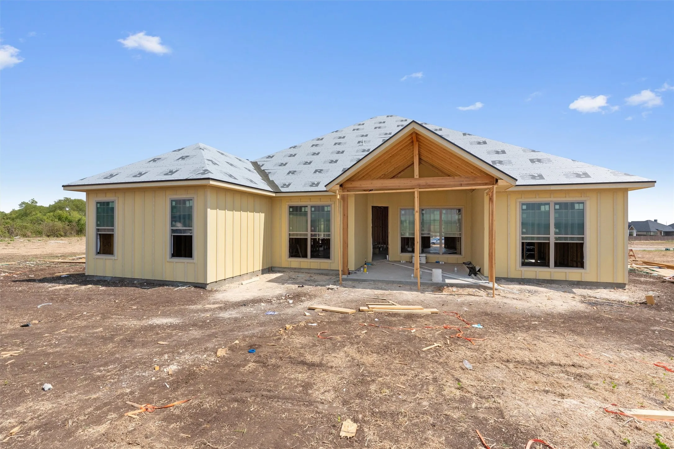 Newly constructed residence featuring light-colored vertical siding, multiple windows, and a covered back patio with exposed wood framing