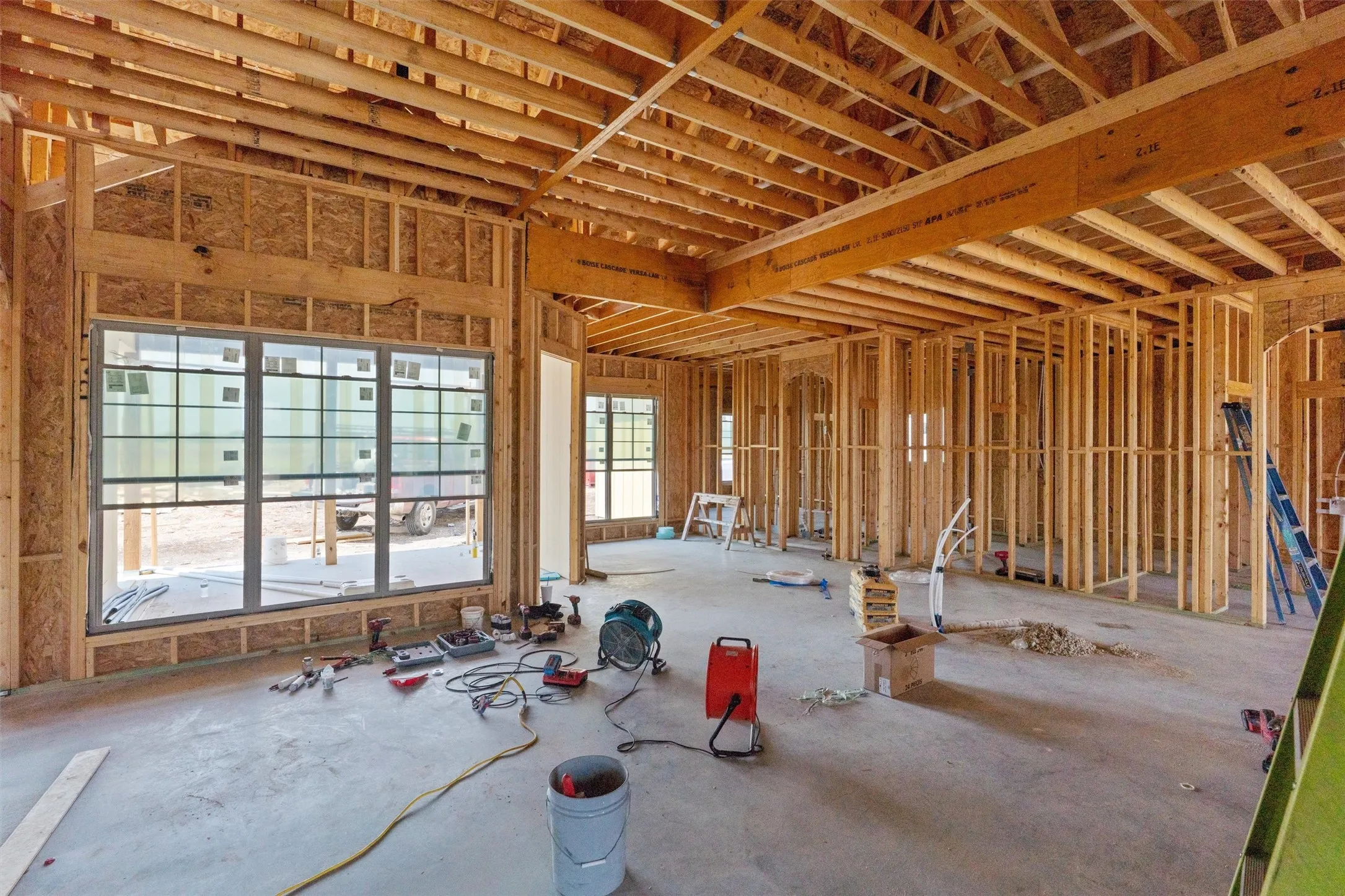 Spacious open-concept layout with concrete slab flooring, wood framing, exposed wood ceiling joists, and large multi-pane windows