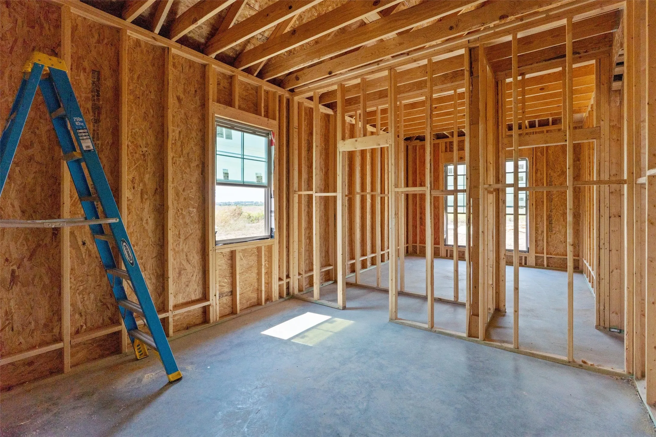 Unfinished interior with exposed wood framing, oriented strand board (OSB) sheathing, concrete flooring, and multiple window openings