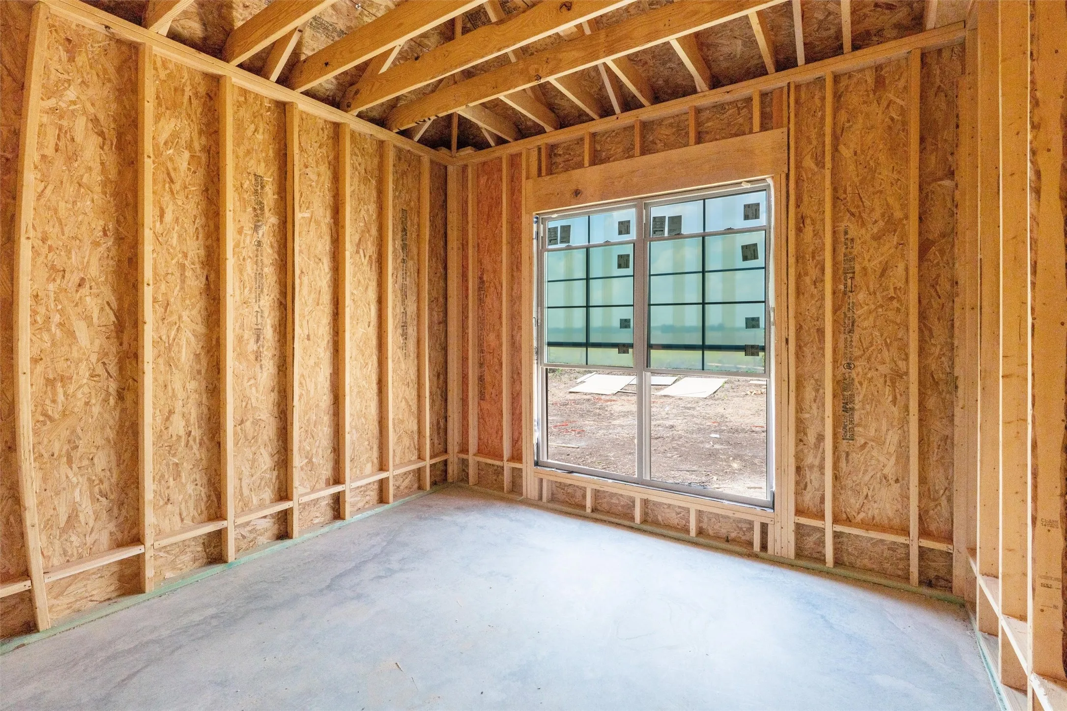 Framed interior space featuring exposed wood studs, oriented strand board sheathing, and a concrete slab foundation