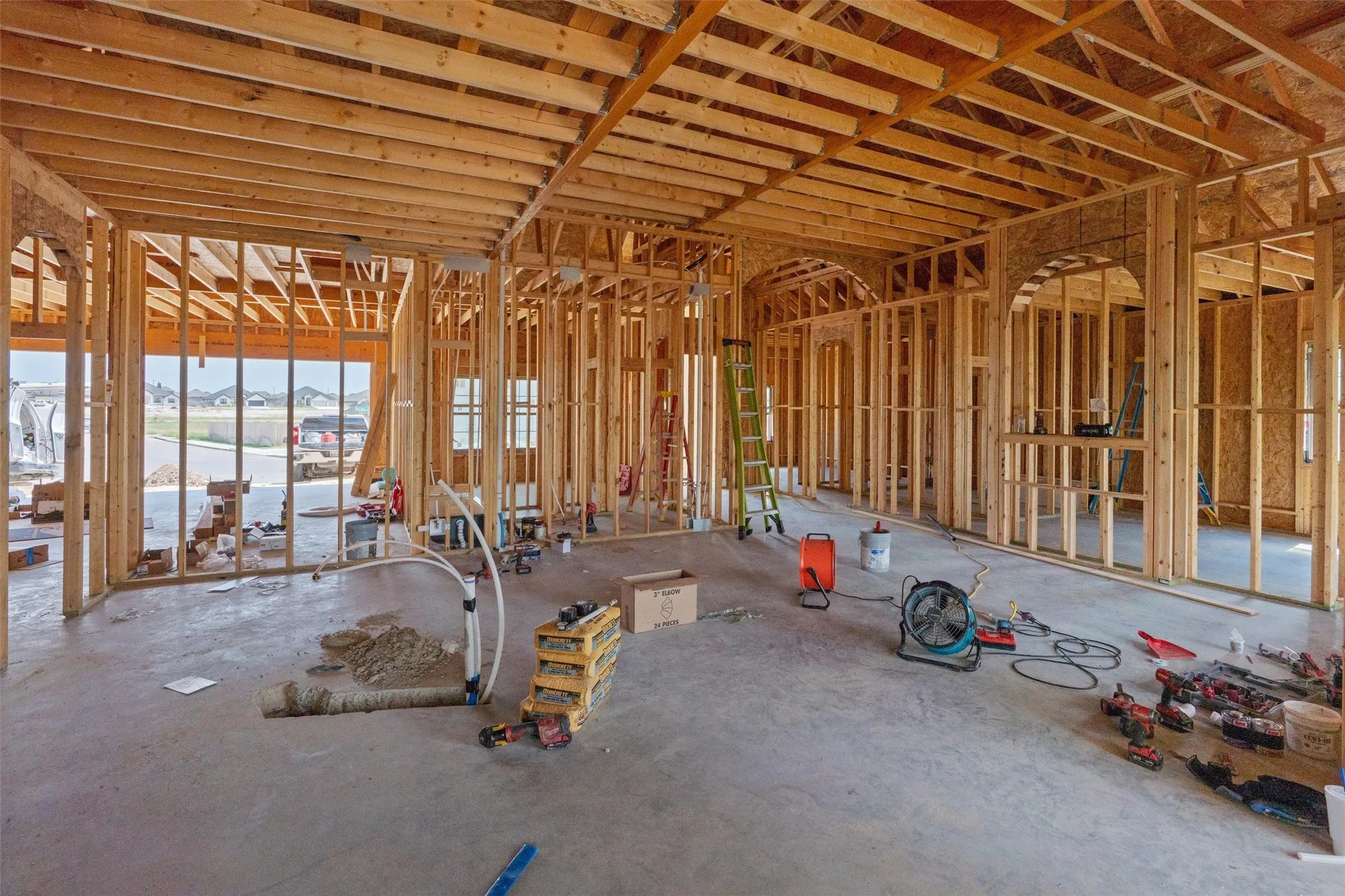 New construction framing with exposed wooden beams, multiple arched wall openings, and concrete flooring