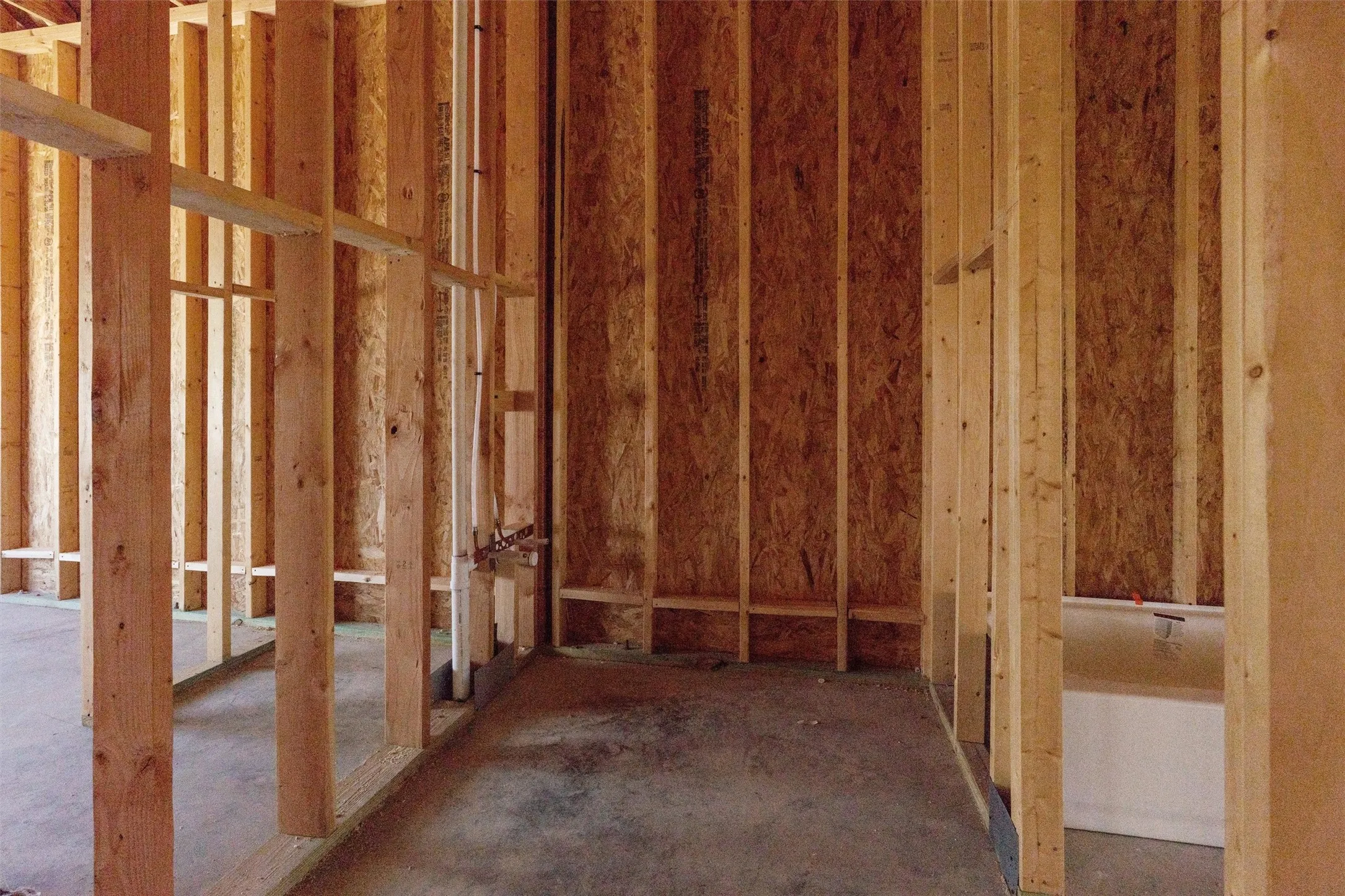 Unfinished interior framing with exposed wood studs, oriented strand board sheathing, visible plumbing lines, and concrete flooring