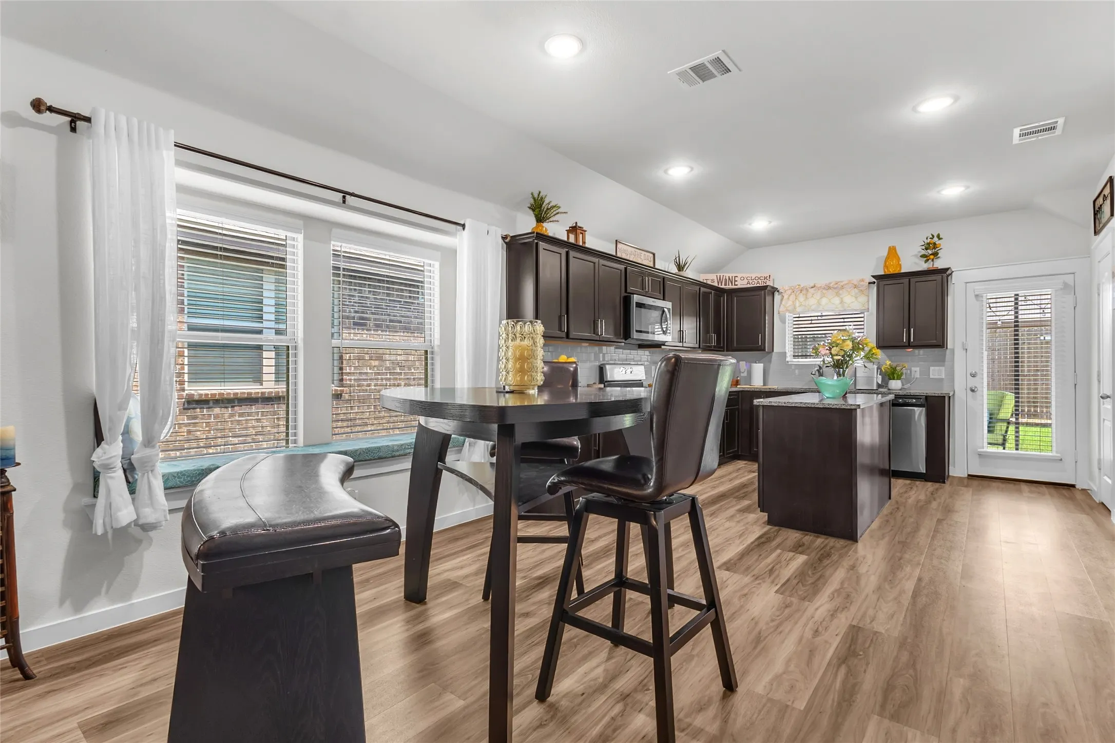 Open-plan kitchen with dark wood cabinetry, quartz countertops, stainless steel appliances, recessed lighting, and large windows providing ample natural light