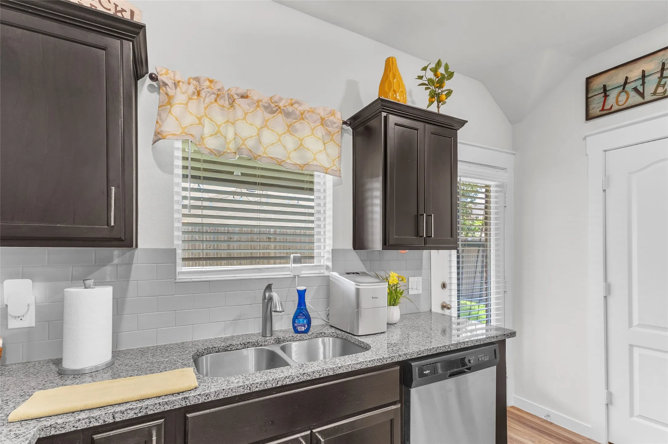 Open-plan kitchen with dark wood cabinetry, granite countertops, stainless steel appliances, and natural light from window treatments.