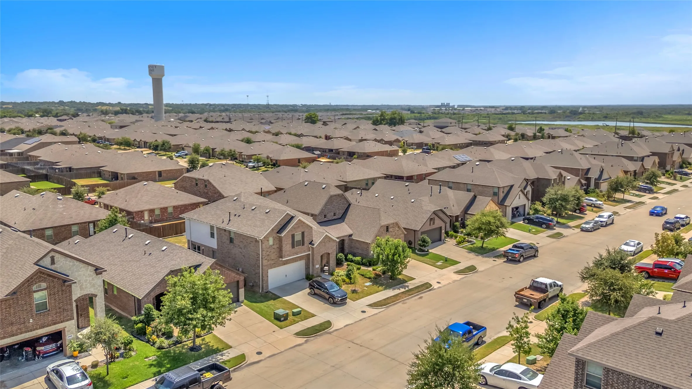 Aerial view of a suburban neighborhood with uniform single-family homes, asphalt driveways, and green lawns, bordered by a water tower in the distance