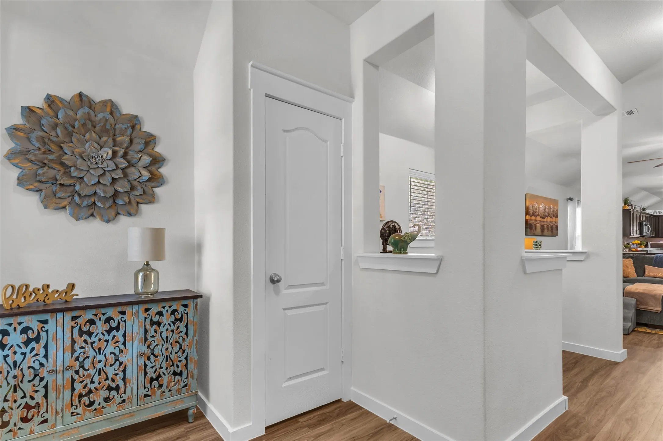 Entryway with white walls, wood laminate flooring, decorative accent wall, and a console table with intricate blue and gold design.