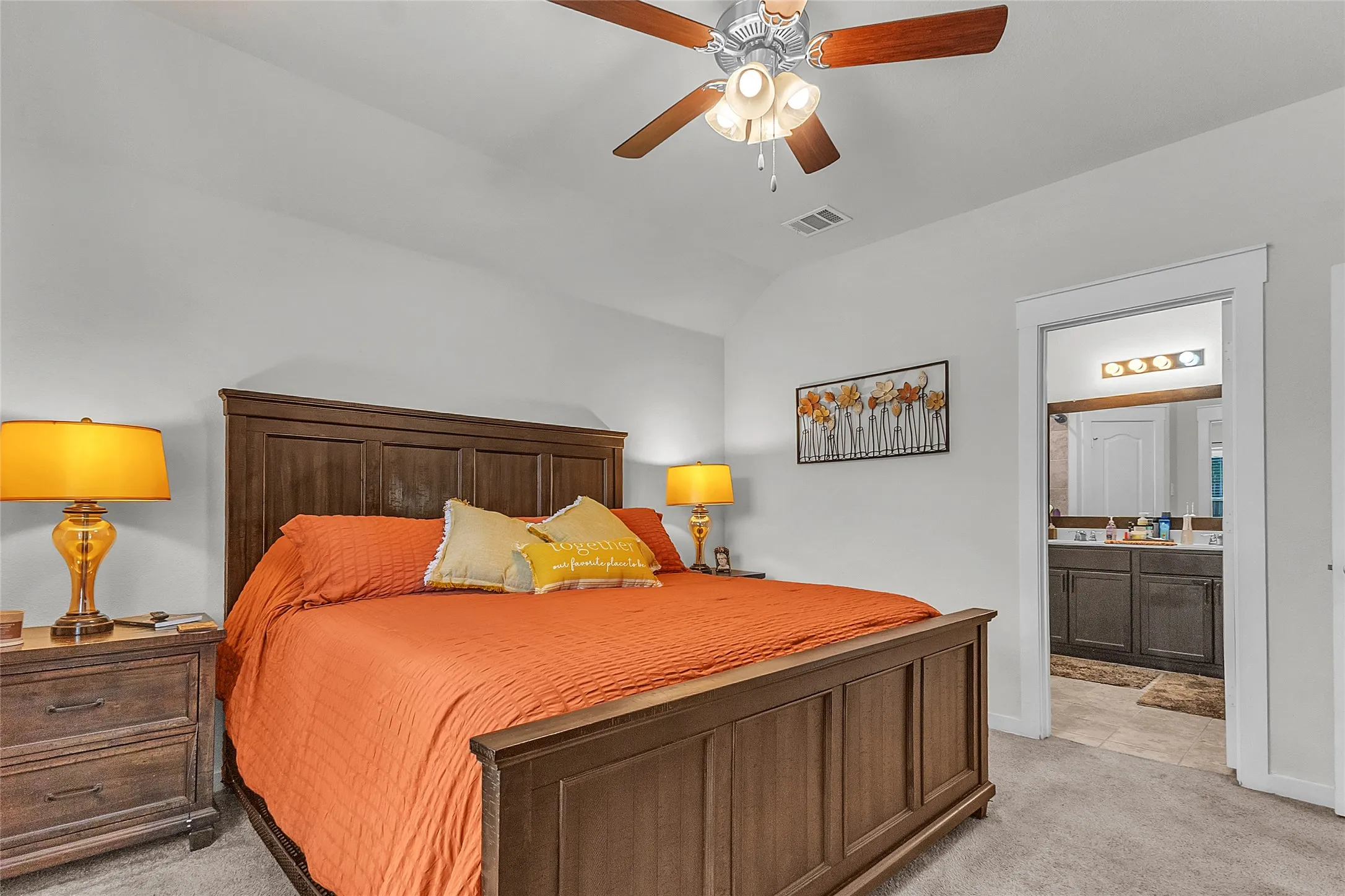 Primary bedroom with hardwood flooring, orange duvet, wooden bed frame, and two vintage lamps beside nightstands, illuminated by natural light from a nearby bathroom.