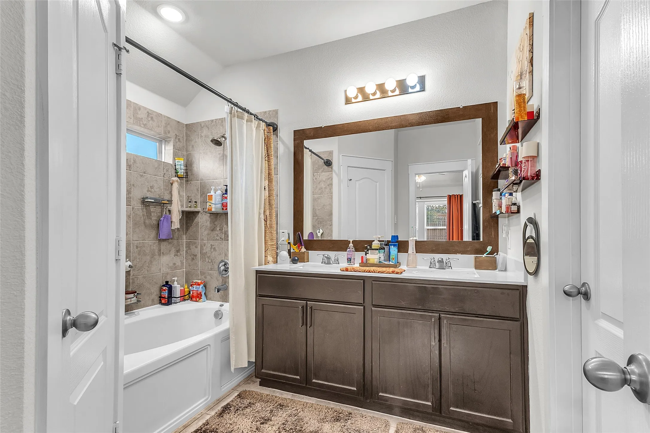 Bathroom with dual sink vanity in dark wood, tub/shower combo with tile surround, and natural light from window opposite the entry.