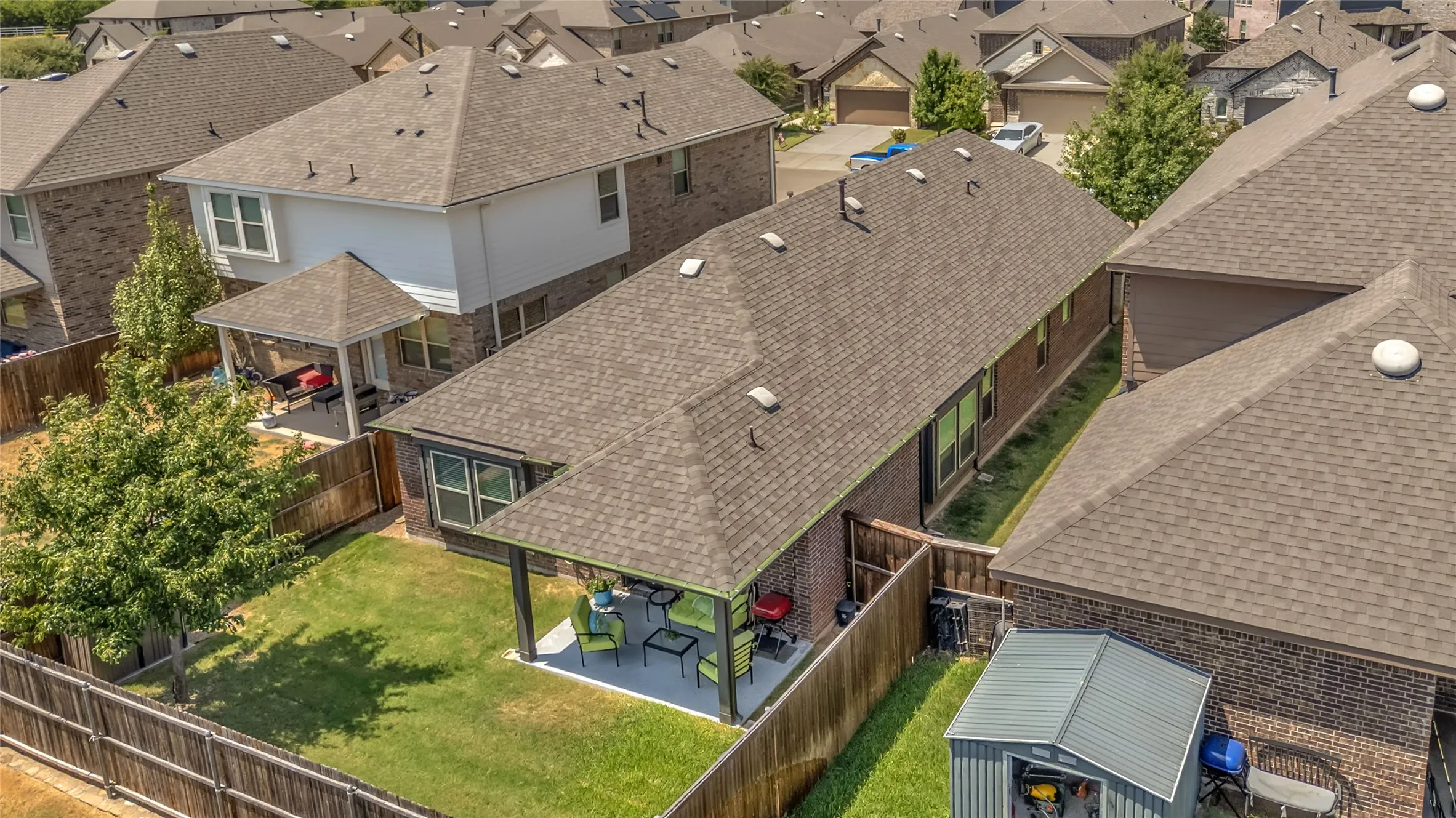 Covered back patio with concrete floor, adjacent to well-maintained lawn, surrounded by wooden privacy fences and residential rooftops.