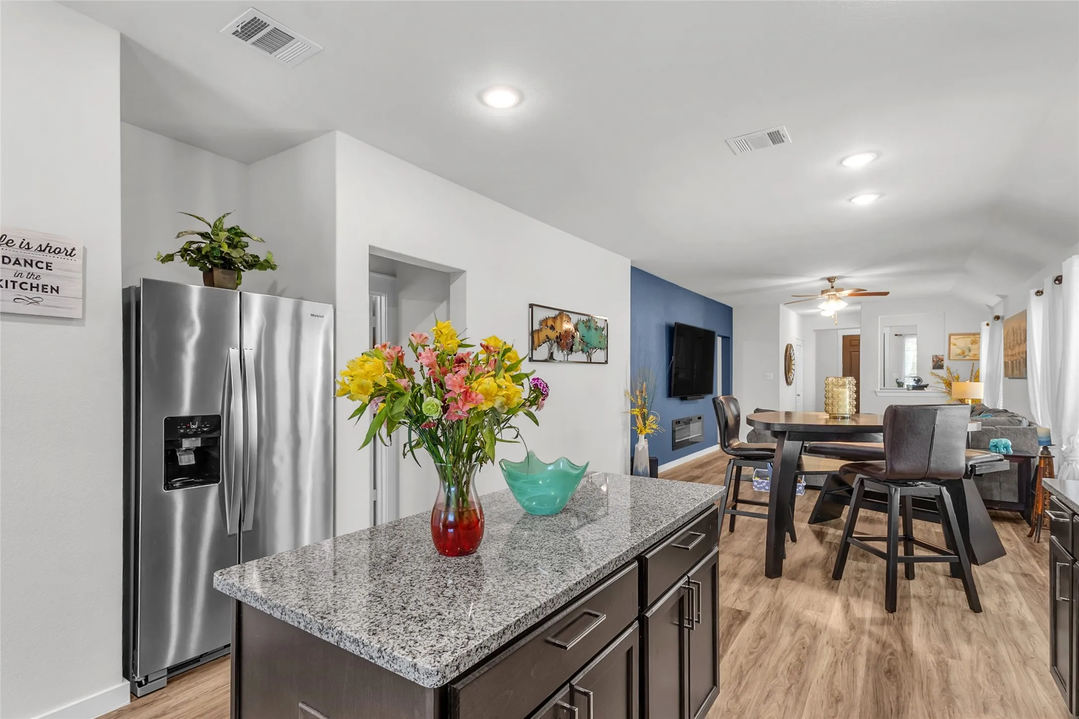 Open-plan kitchen with granite countertops, stainless steel appliances, light hardwood flooring, and recessed lighting leading to the dining area.