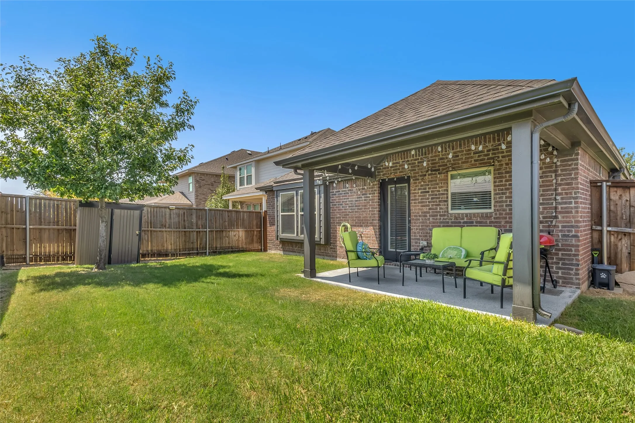 Covered back patio with green seating, concrete flooring, and surrounding privacy fence in a well-maintained lawn area.