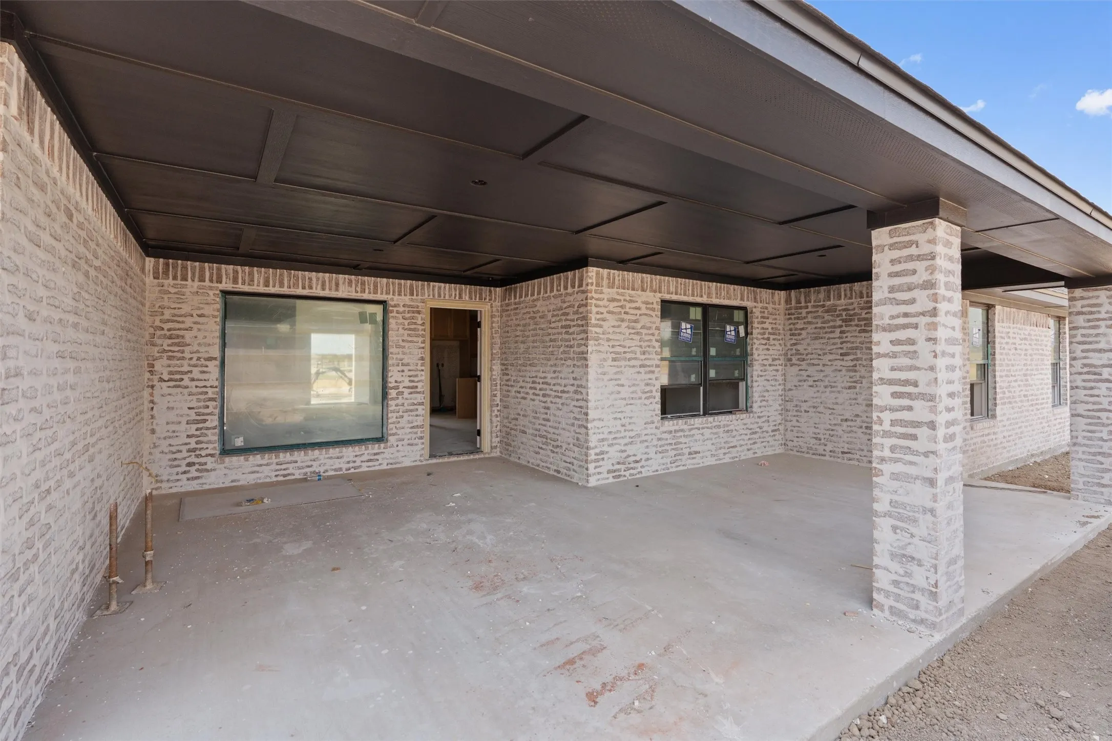 Covered patio with a paneled ceiling, light-toned brick exterior, and a large fixed window