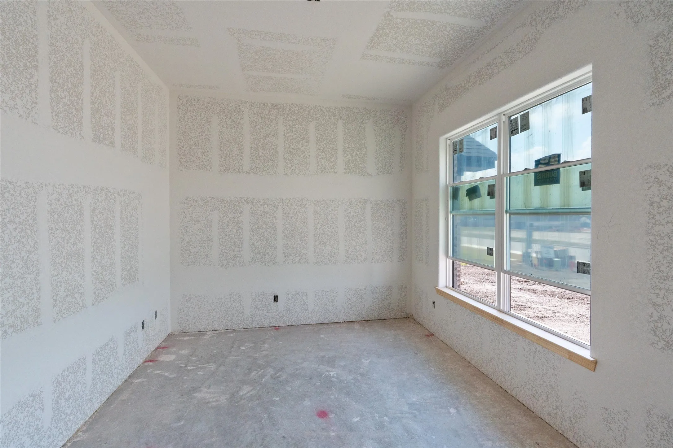 Unfinished interior space featuring drywall installation and a large window with multiple panes