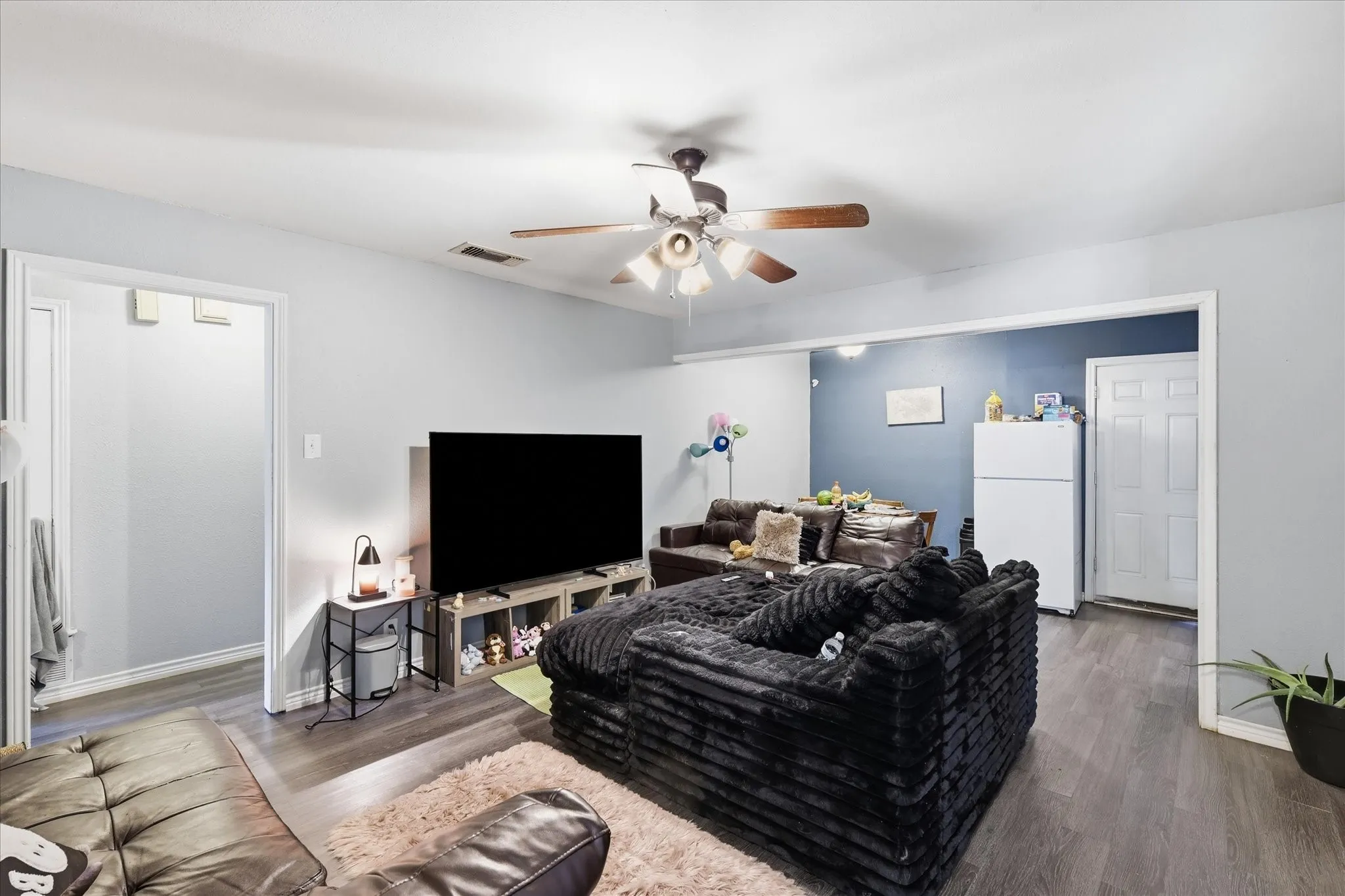 Wood-finish flooring throughout, ceiling fan with integrated lighting, and a white paneled interior door