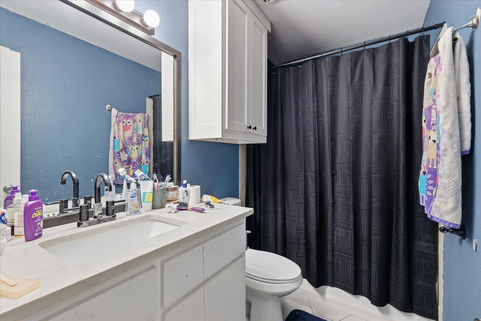 Bathroom featuring a vanity with an integrated sink, wall-mounted light fixture, and white cabinetry