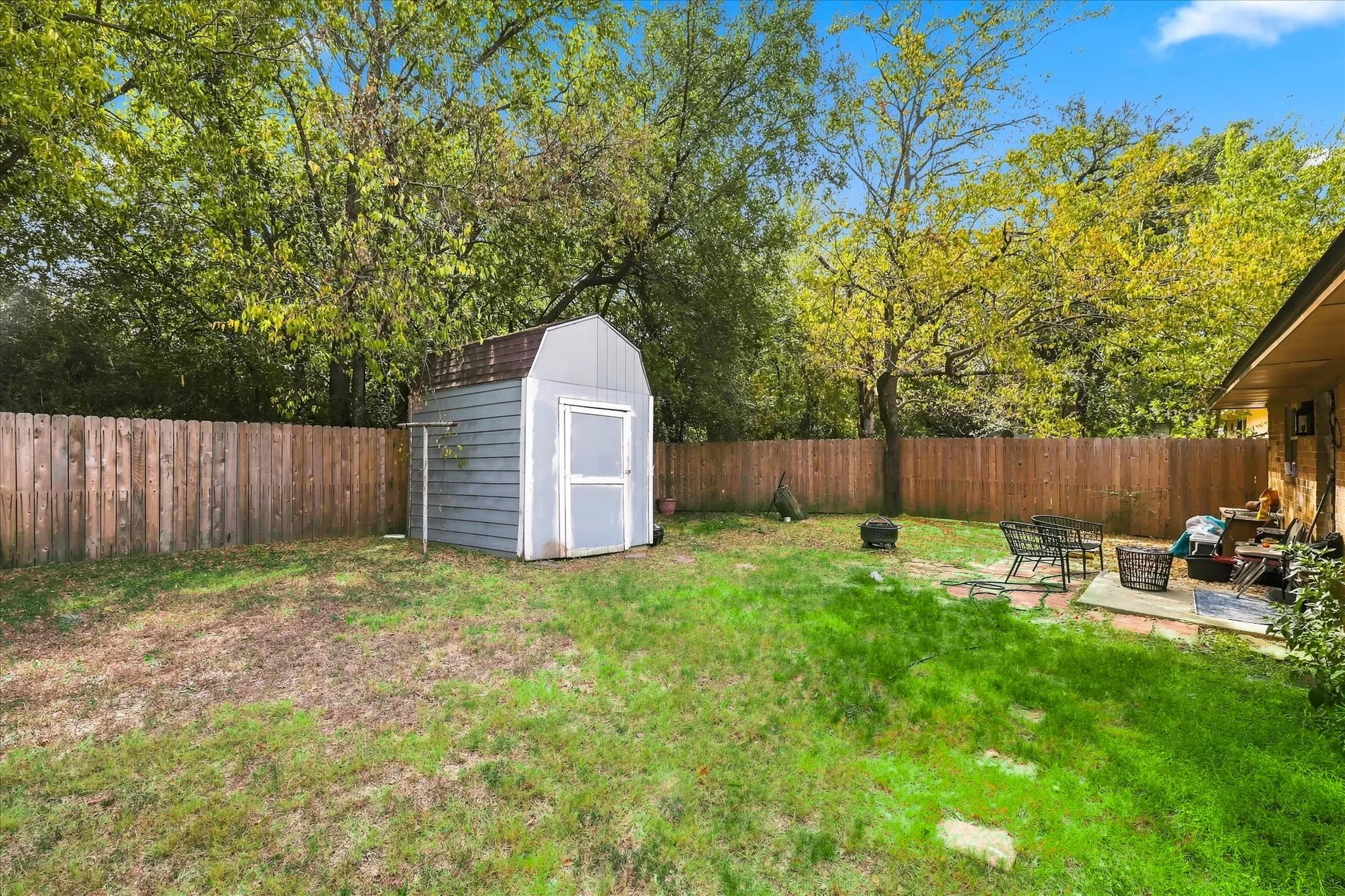 Expansive backyard featuring a wood privacy fence, detached storage shed, and a stone patio