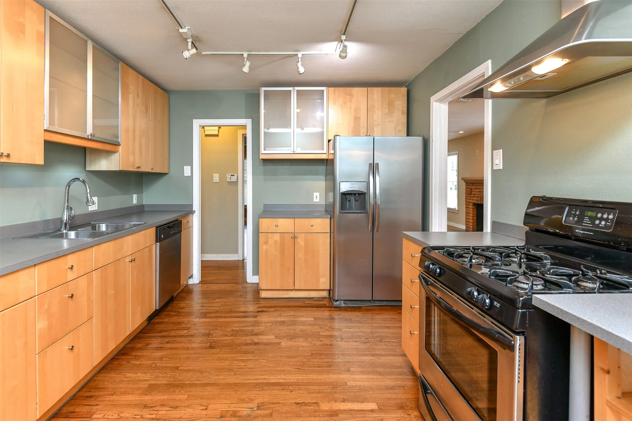 Kitchen featuring rail lighting, stainless steel appliances, sink, wall chimney range hood, and light hardwood / wood-style floors